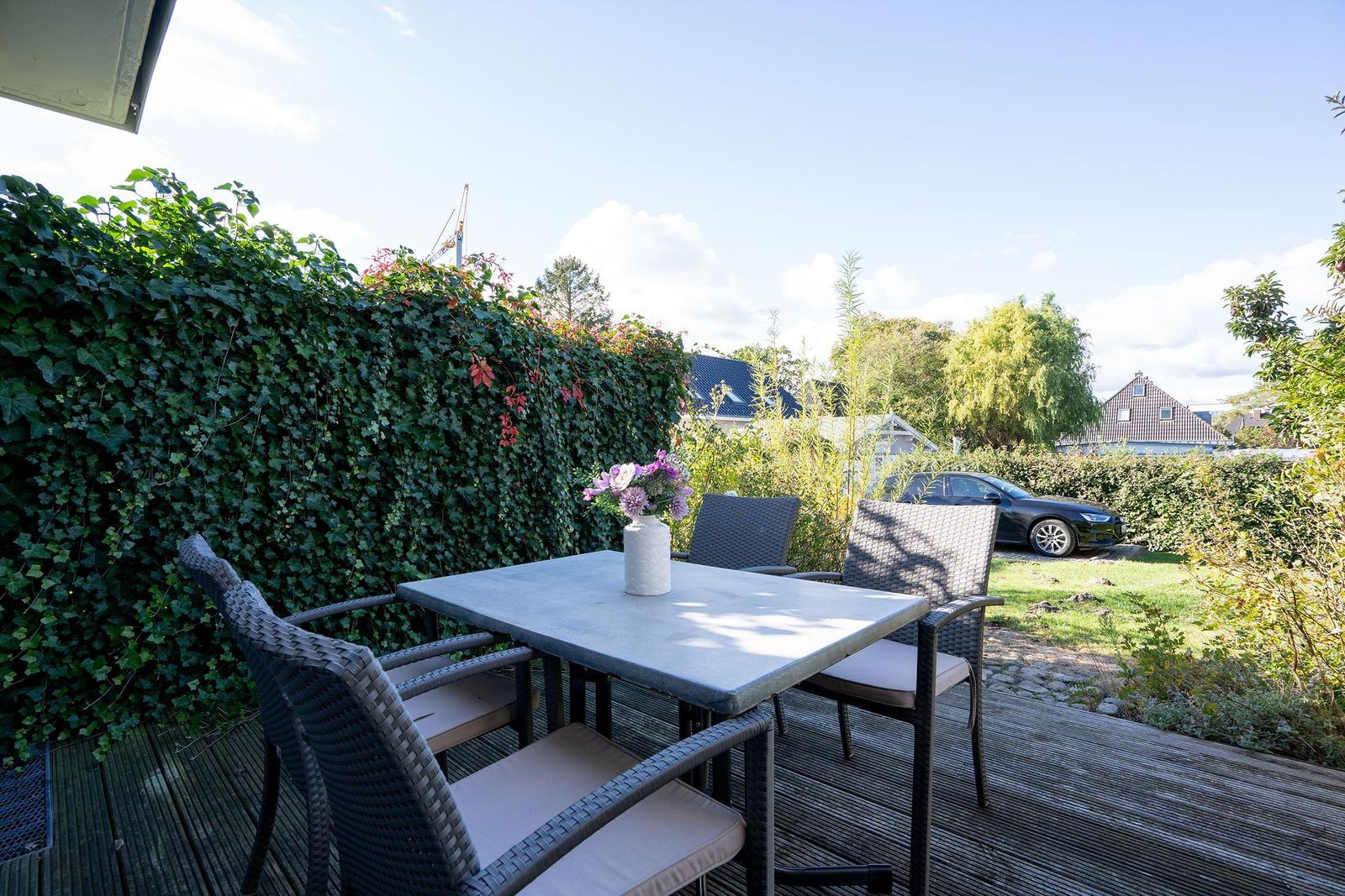 Terrasse mit Tisch und Stühlen, umgeben von grüner Hecke und Garten.