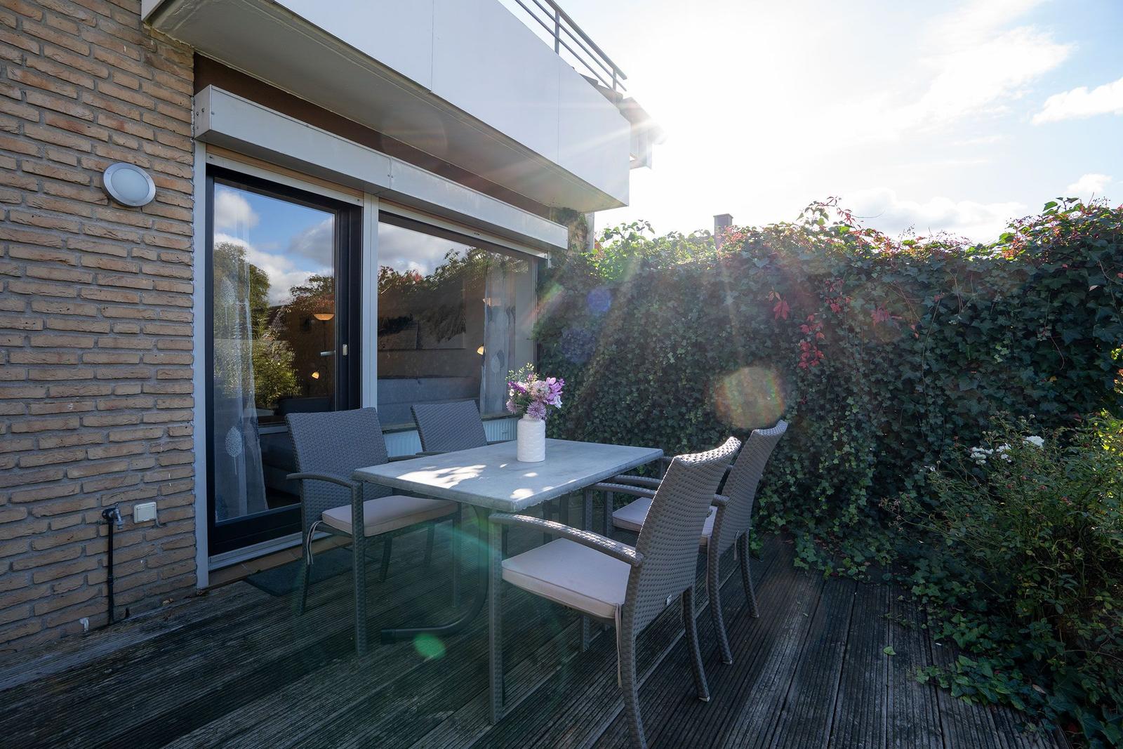 Terrasse mit Tisch und Stühlen, umgeben von grüner Hecke und Sonnenschein.