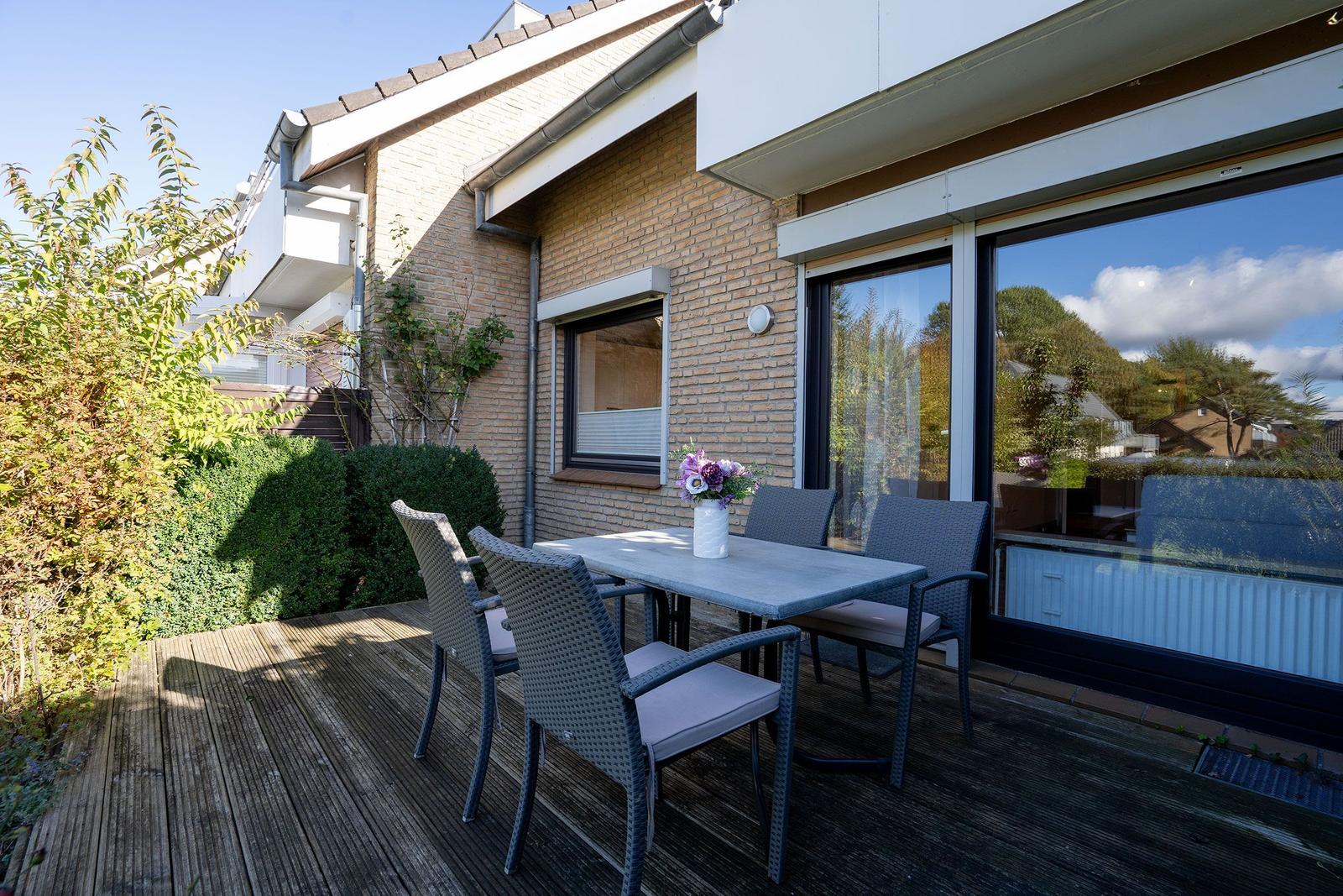 Terrasse mit Tisch und Stühlen, Holzdecke, Blumen und Blick auf Hauswand.