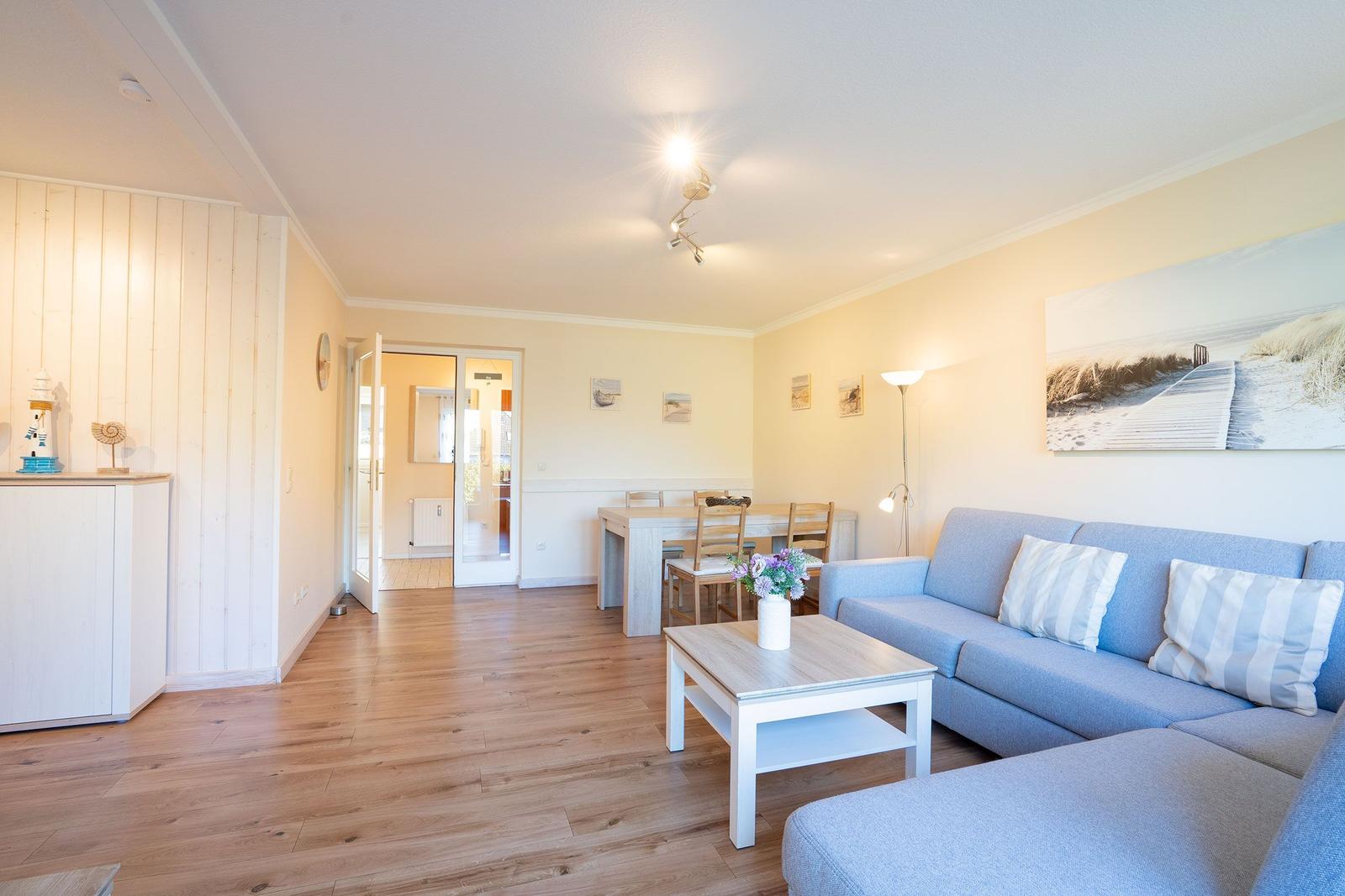 Wohnzimmer mit Sofa, Esstisch und Holzboden. Wandbild und Beleuchtung sichtbar.