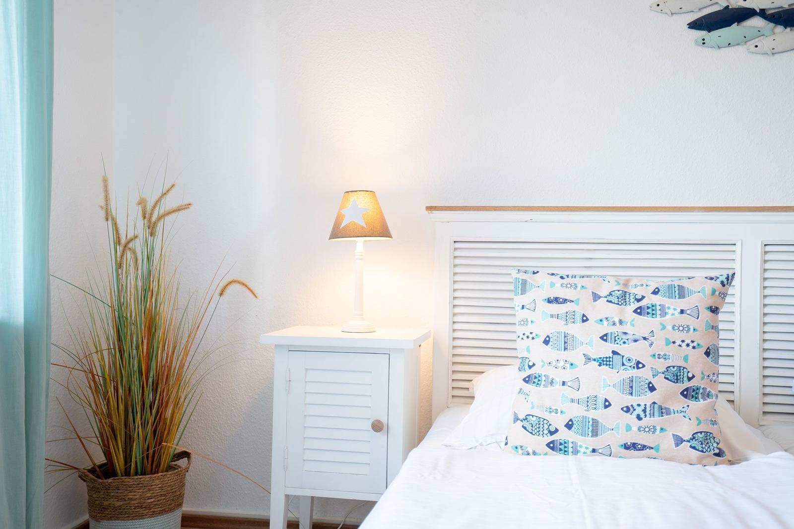 Ein Bett mit Fischkissen, Nachttisch und Lampe neben einer Pflanze.