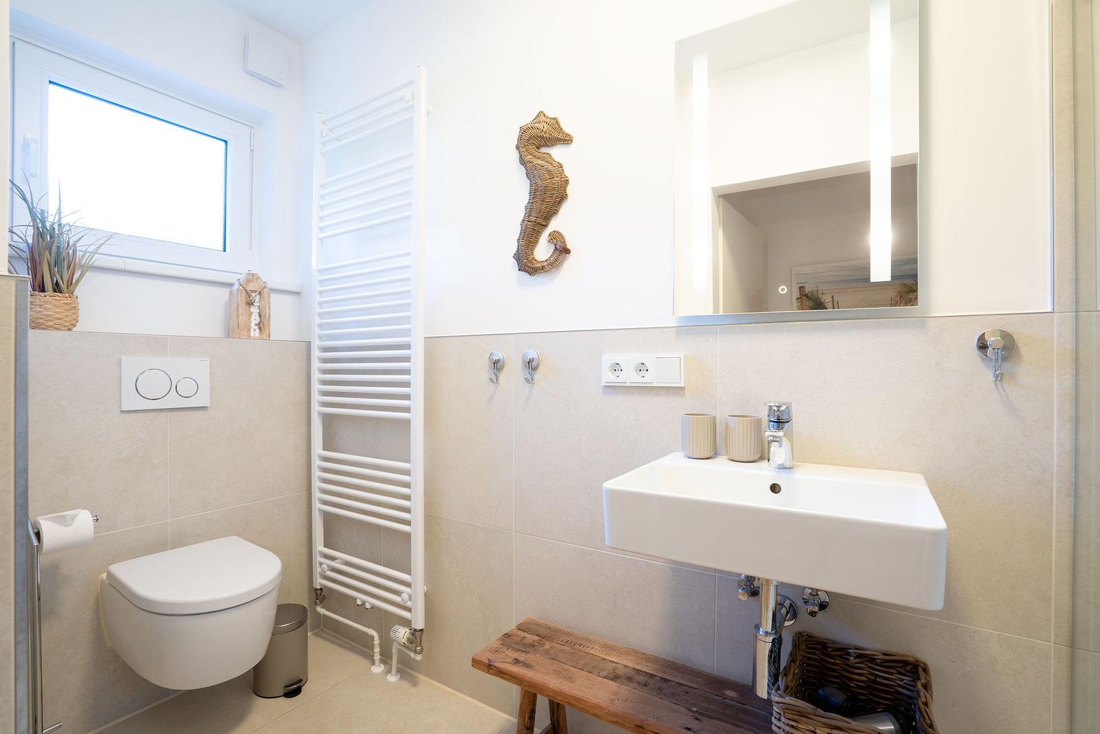Badezimmer mit Waschbecken, Spiegel, Toilette und Heizkörper.