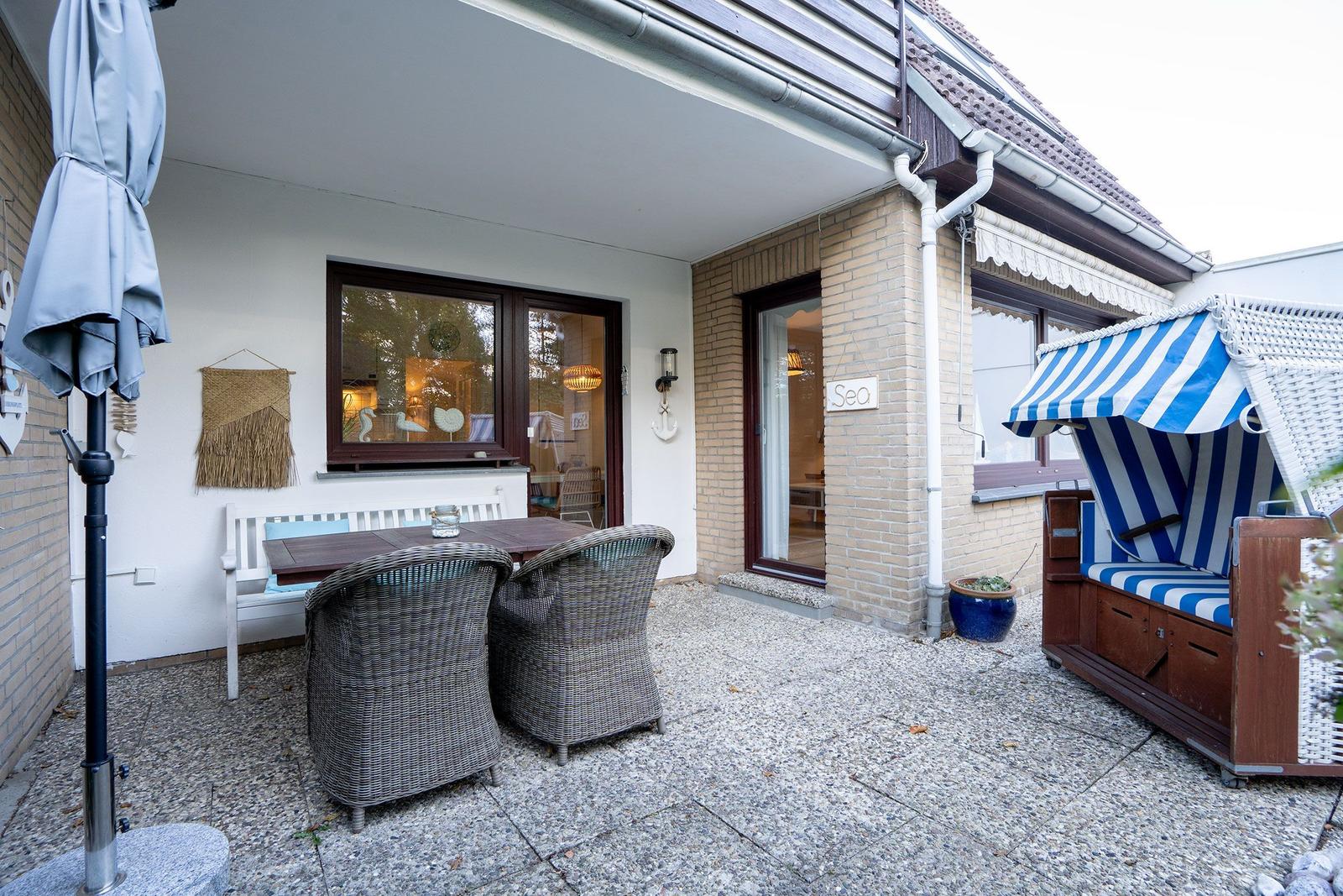 Terrasse mit Tisch, Stühlen und Strandkorb. Durchgang zur Wohnung.