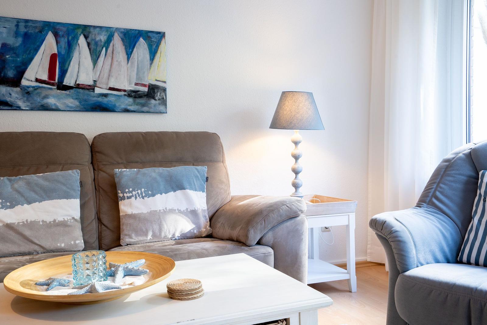 Ein Wohnzimmer mit Sofa, Sessel, Tisch und Wandbild mit Segelbooten.