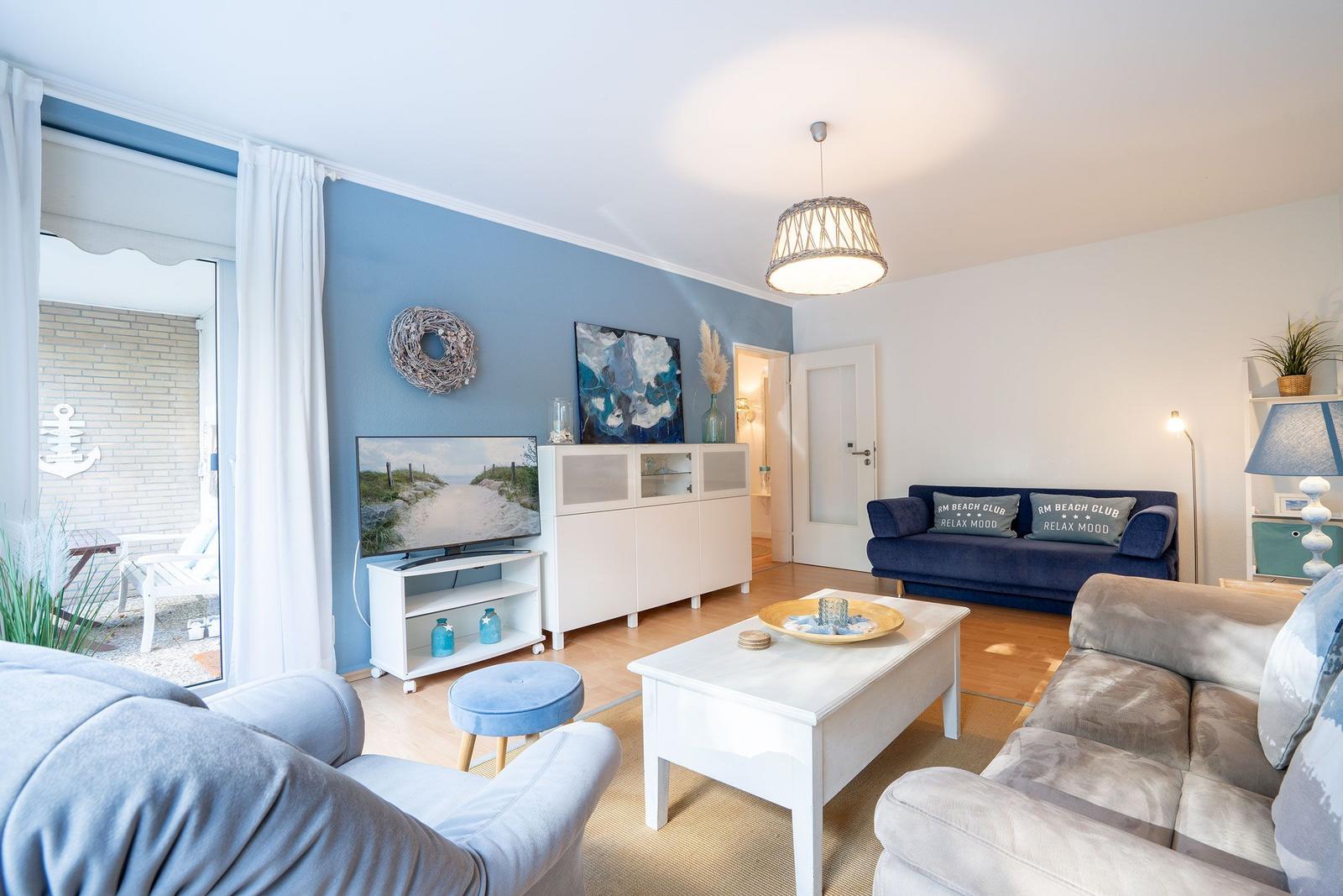 Wohnzimmer mit blauer Wand, Sofa, Couch und TV. Durchgang zur Terrasse.