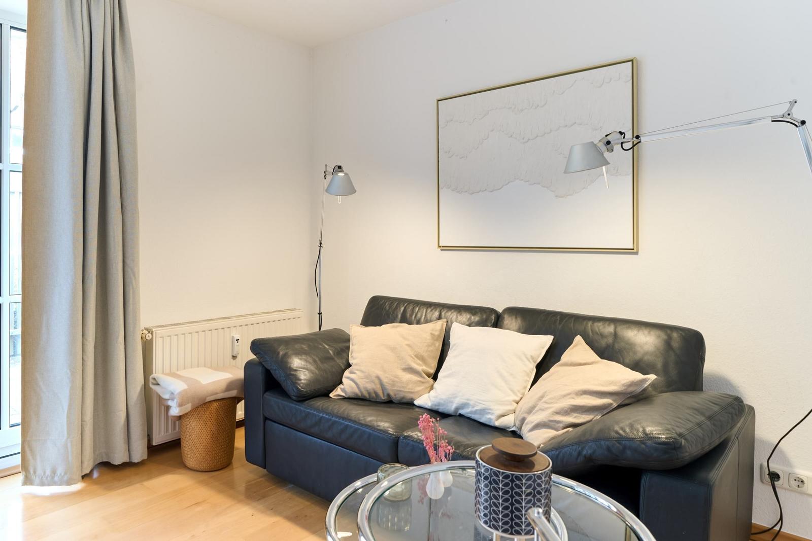 Ein Wohnzimmer mit einem schwarzen Sofa, einer Glasplatte und einer Wandlampe.