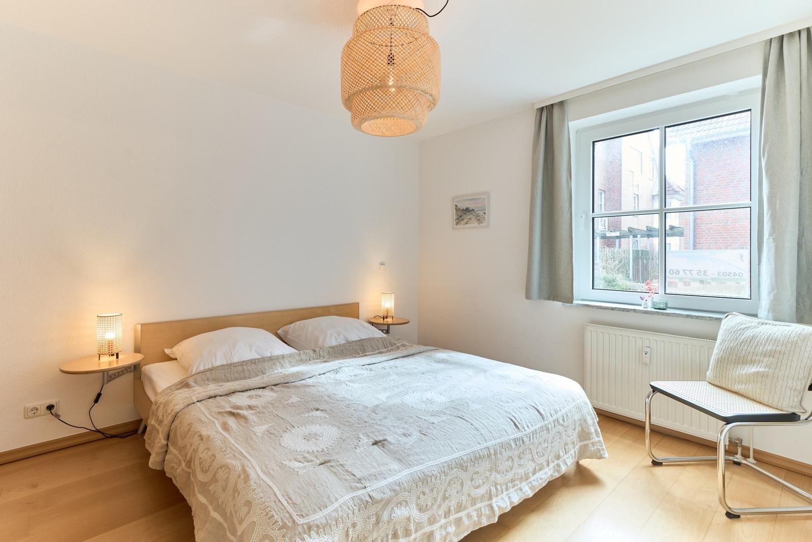 Schlafzimmer mit Bett, Nachttischen, Lampe und Fenster. Holzfußboden und Deckenleuchte.