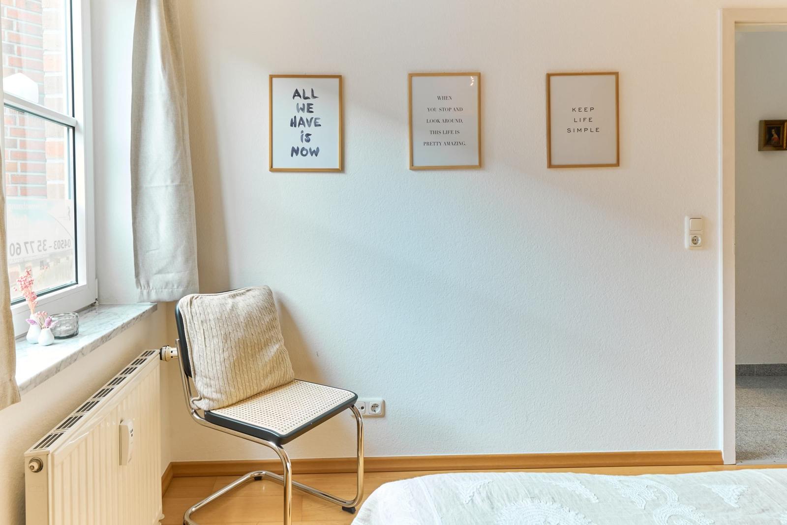 Ein Zimmer mit Stuhl, Fenster und drei Wandbilder.