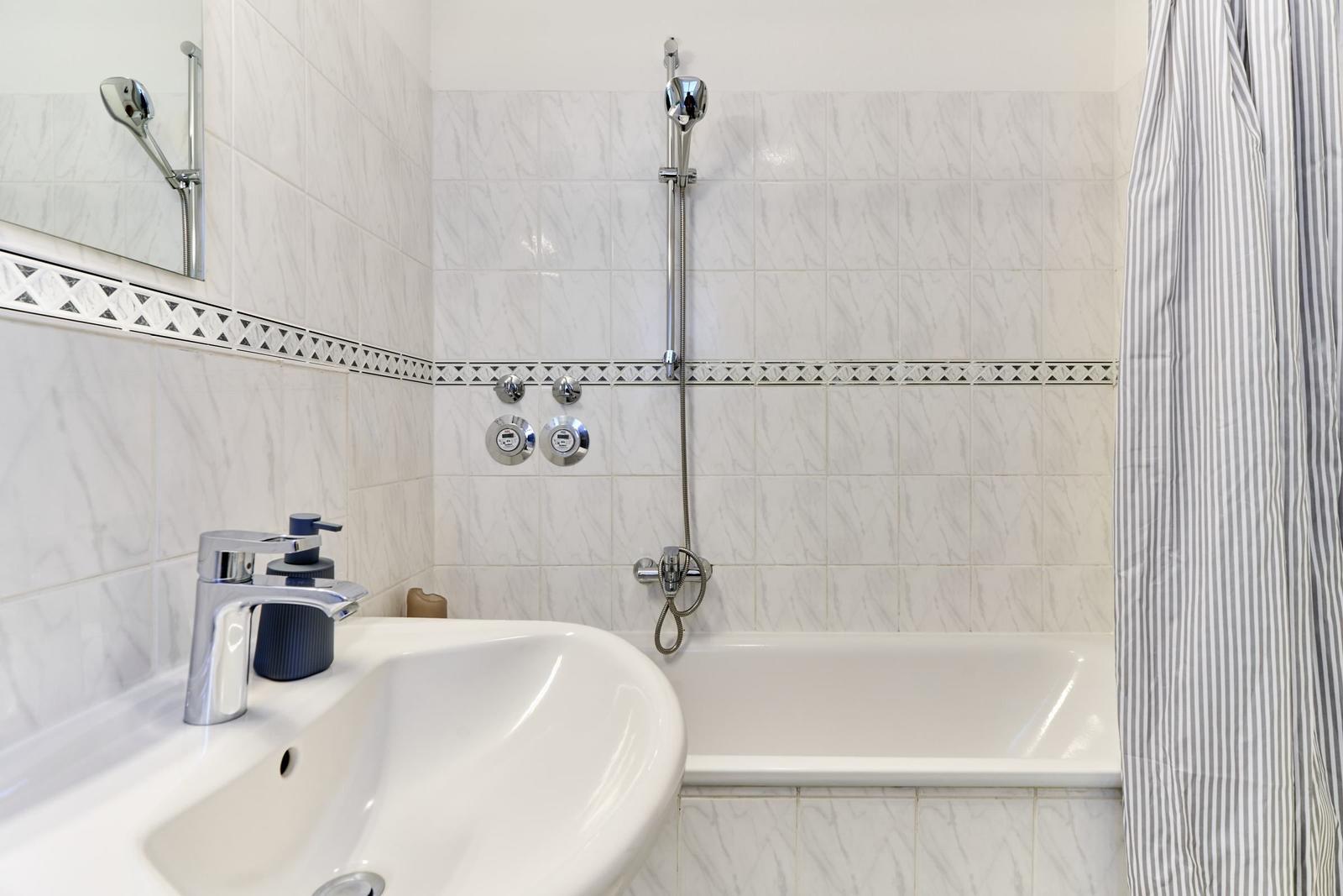 Badezimmer mit Badewanne, Dusche und Waschbecken. Fliesen mit Musterband.