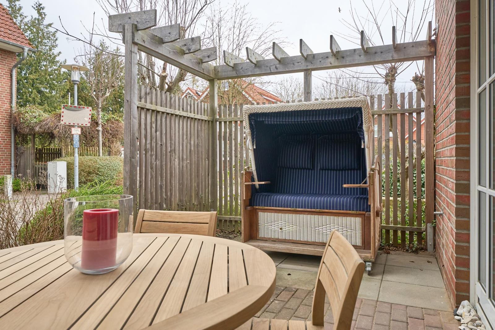 Terrasse mit Holztisch, Stühlen und Strandkorb unter Holzüberdachung.