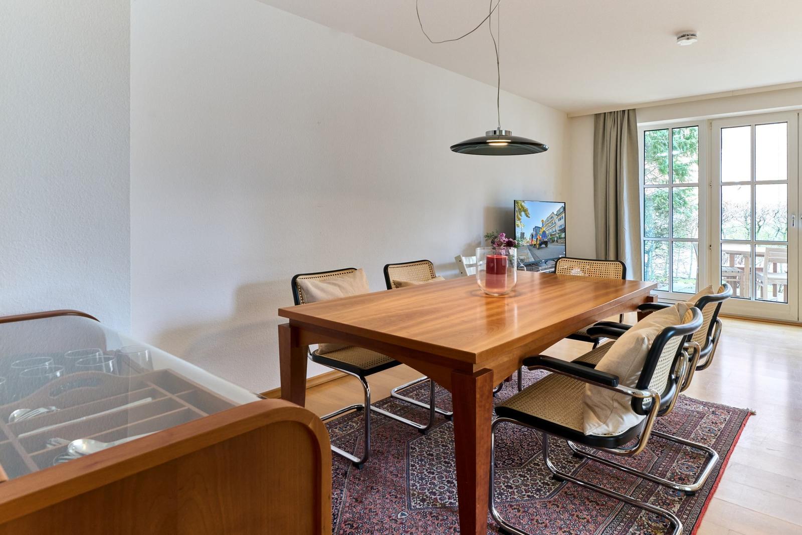 Esszimmer mit Holztisch, Stühlen und TV. Fenster zur Terrasse.