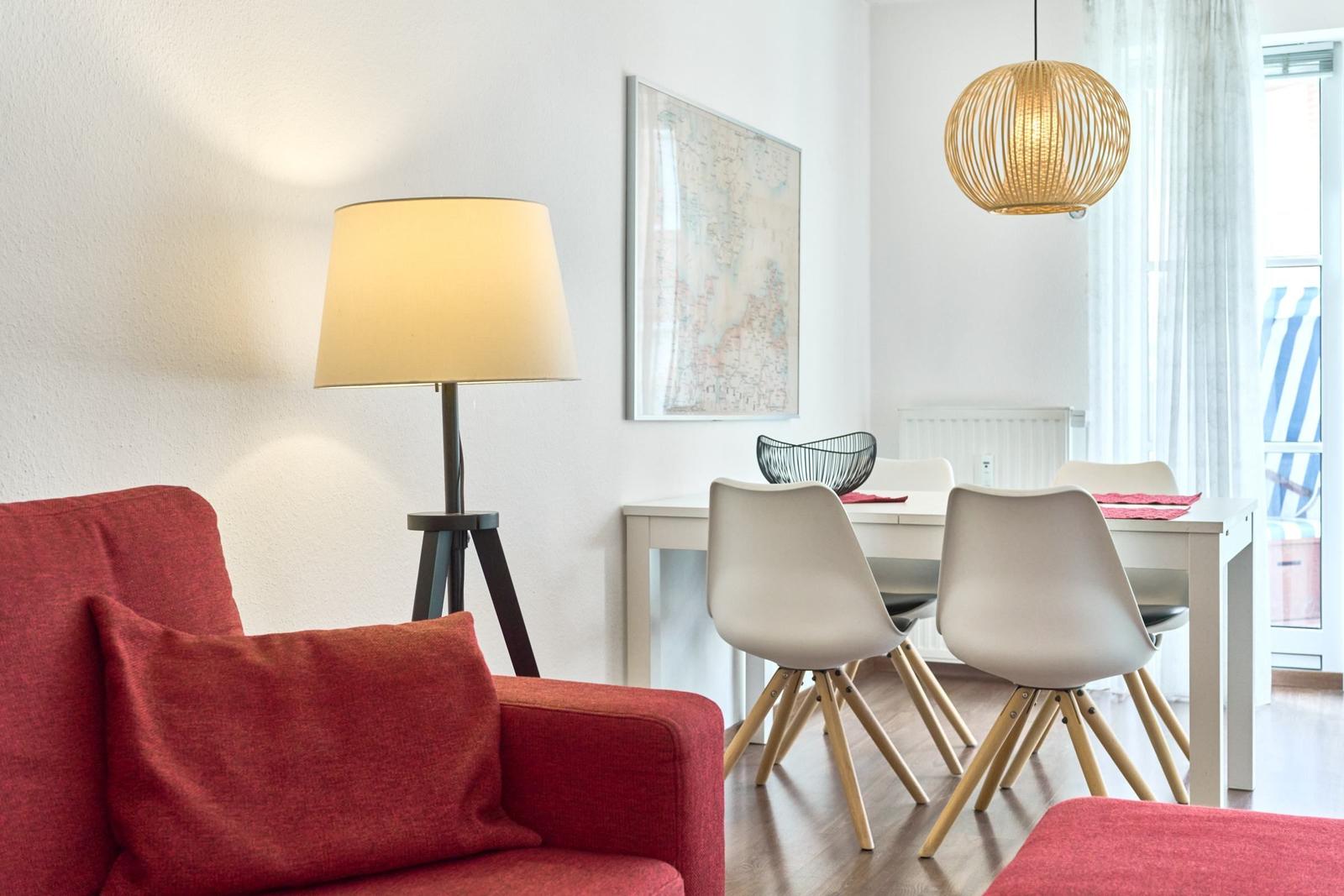 Rotes Sofa, Esstisch mit Stühlen, Stehlampe und Hängelampe im Raum.