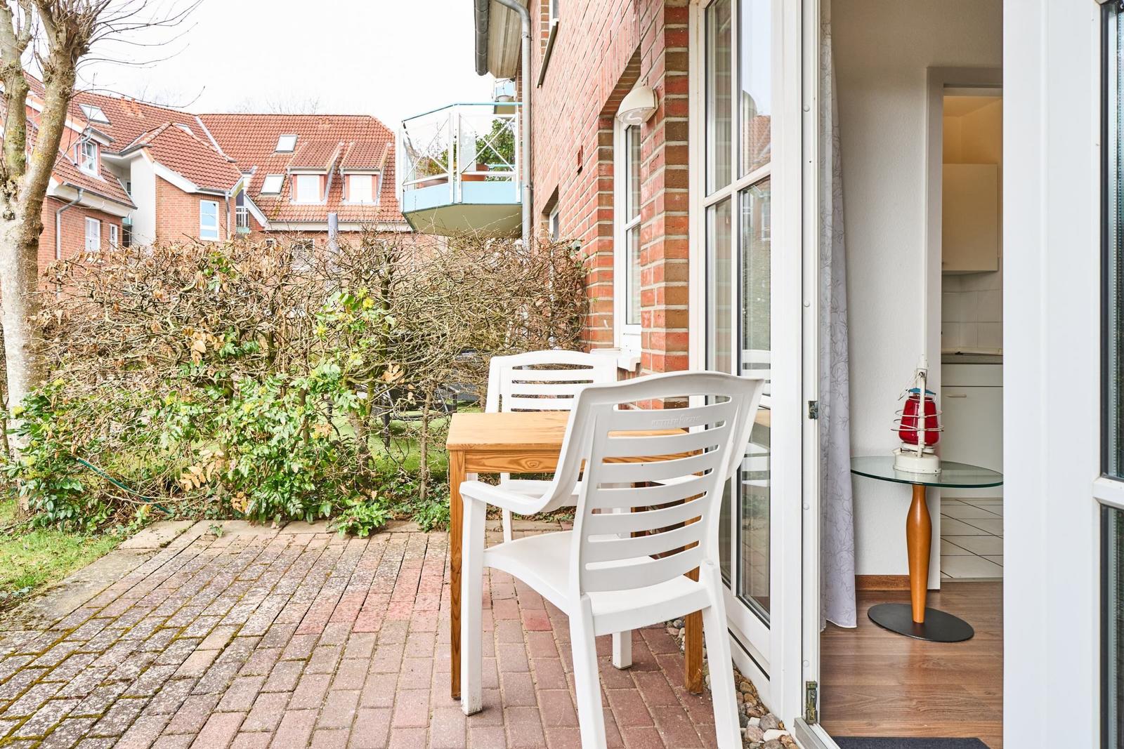 Terrasse mit Tisch und Stühlen, Blick auf Garten und benachbarte Häuser.