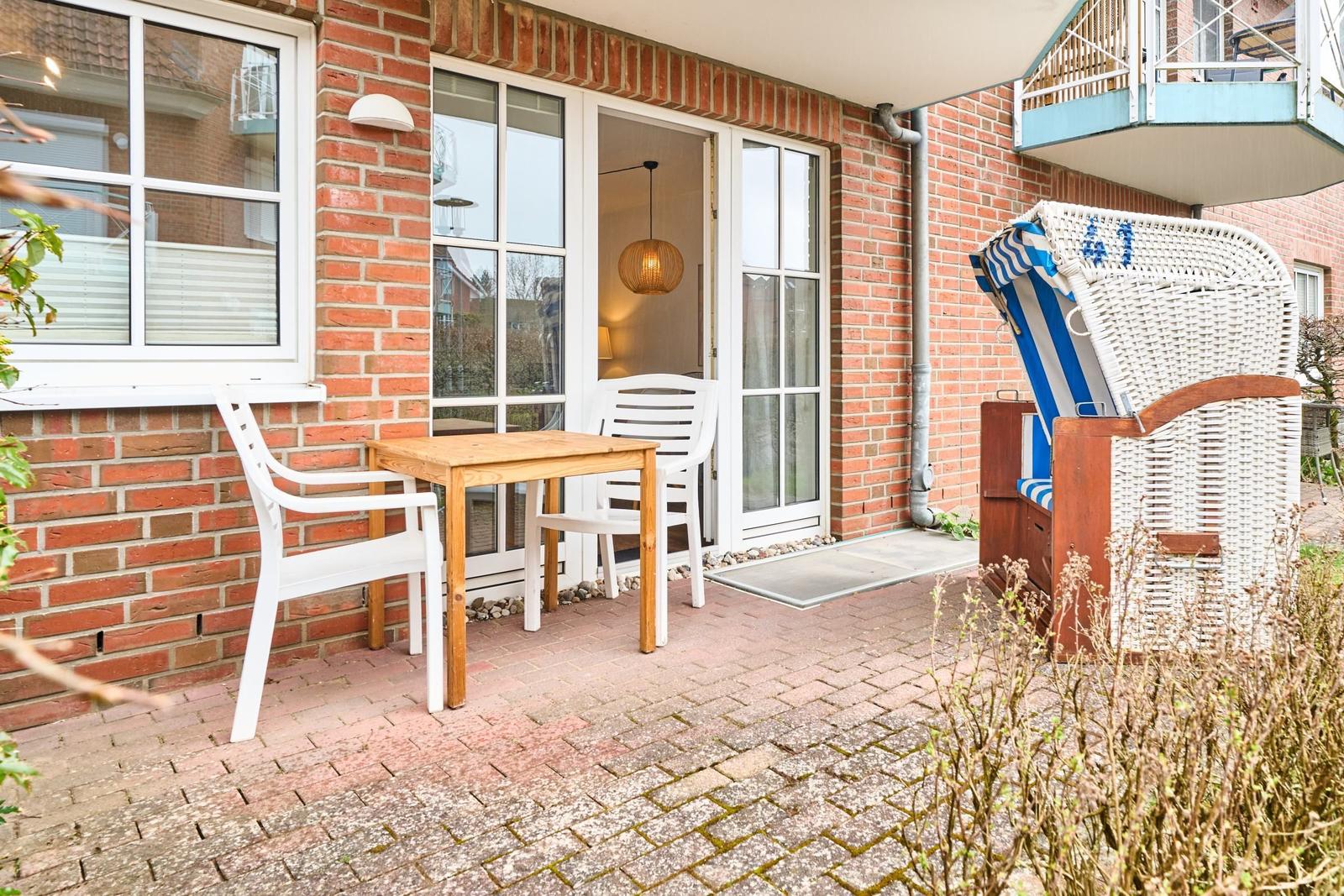 Terrasse mit Tisch, Stühlen und Strandkorb. Durchgang zur Wohnung.