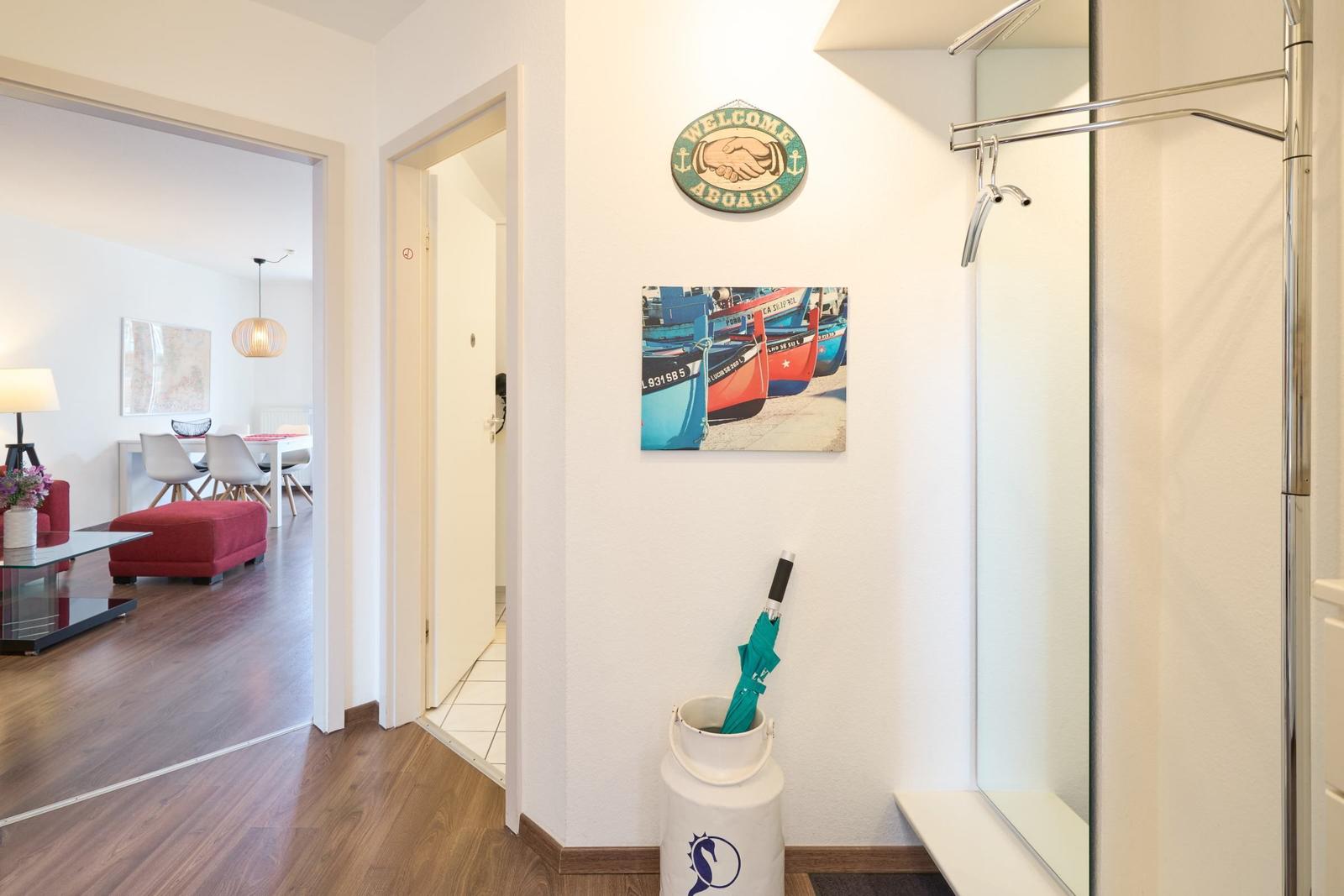 Flur mit Dusche, Wandbild und Willkommensschild. Blick in Wohn- und Essbereich.