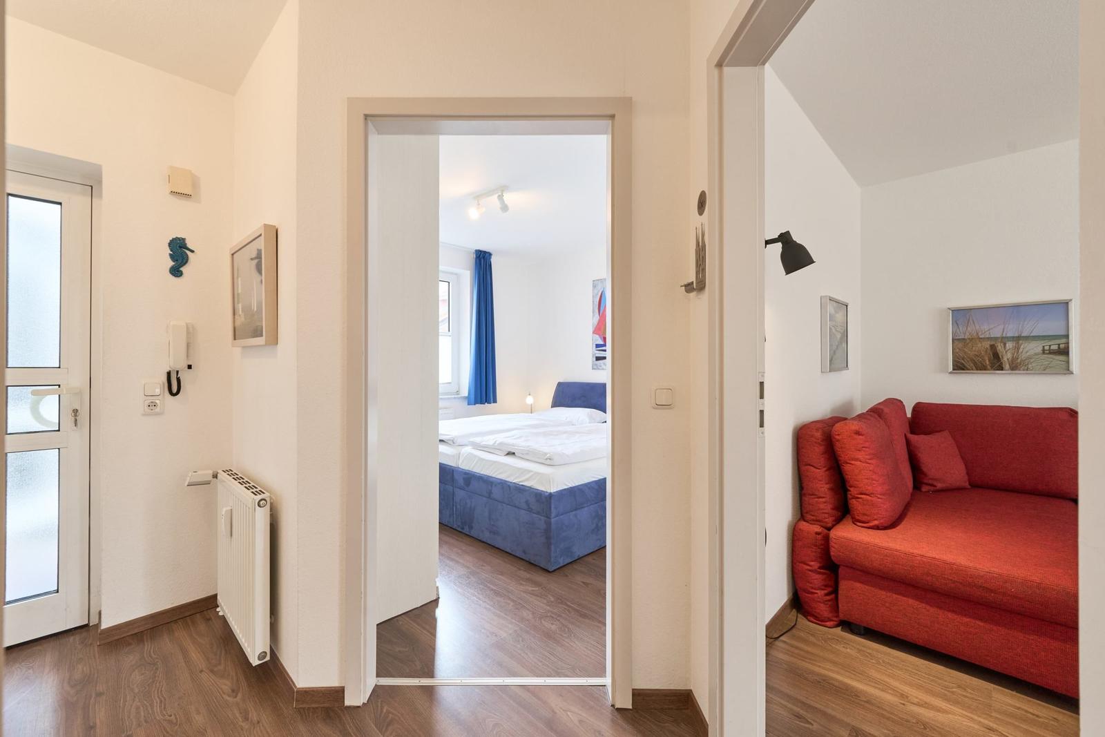 Haus mit Wohnzimmer, rotem Sofa und Schlafzimmer mit blauem Bett.