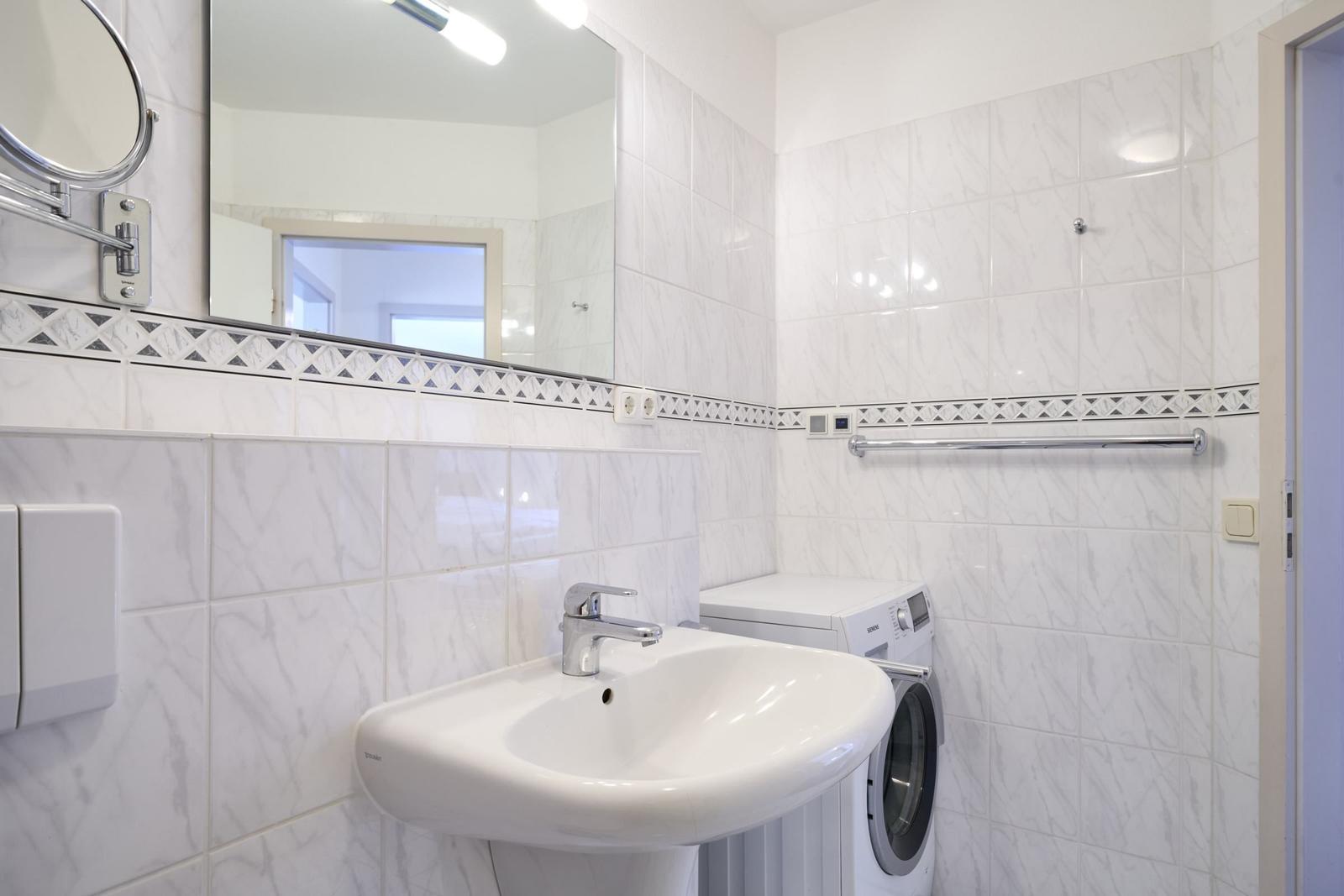 Badezimmer mit Waschbecken, Spiegel und Waschmaschine.
