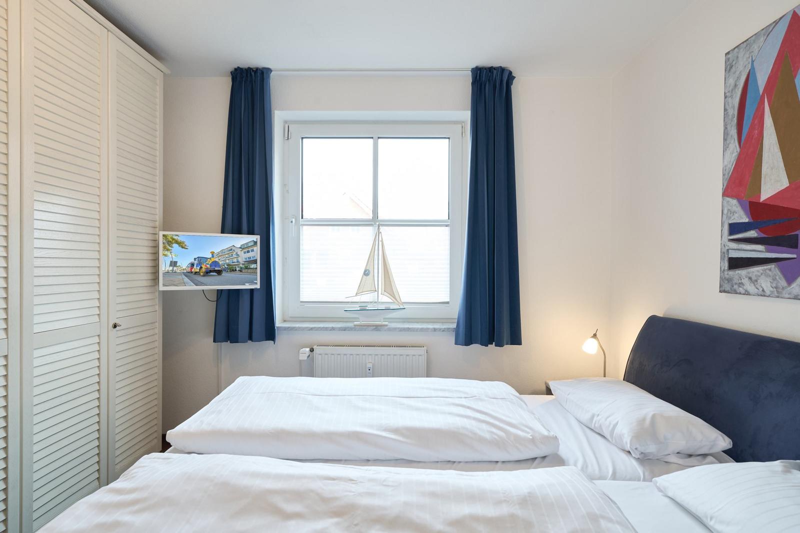 Schlafzimmer mit Bett, Fenster, Vorhängen und Wandbild.