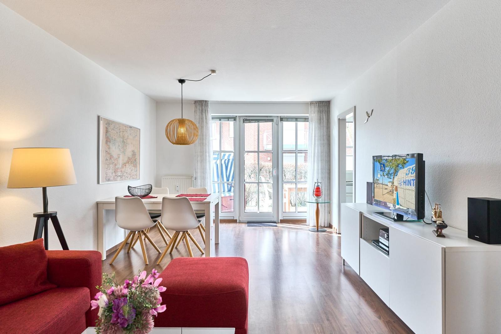 Wohn- und Essbereich mit rotem Sofa, Tisch und Stühlen, TV und Blick auf Balkon.