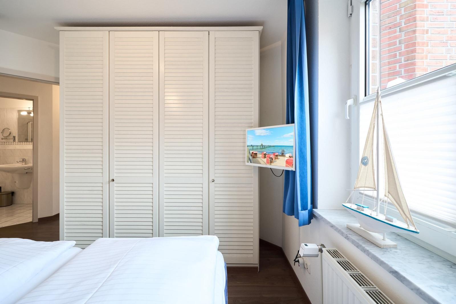 Schlafzimmer mit weißem Schrank, Bett und Fenster mit Segelschiffmodell.