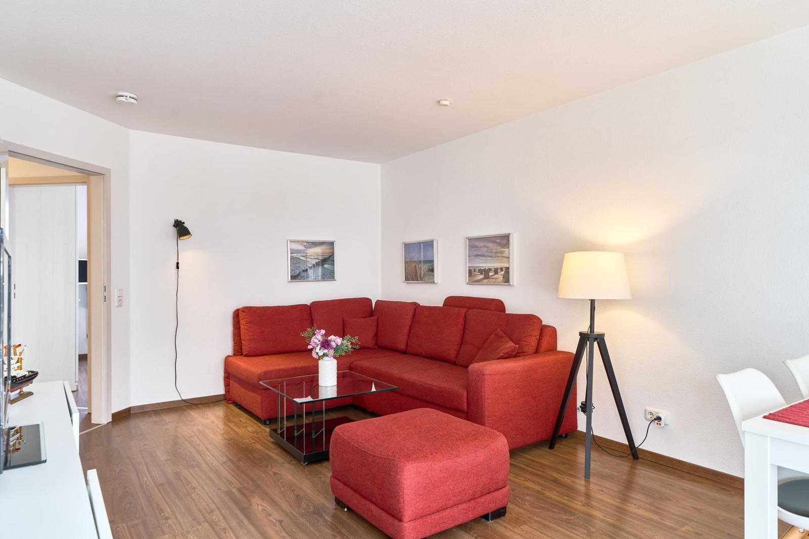 Ein Wohnzimmer mit rotem Sofa, Glas-Tisch und Stehlampe.