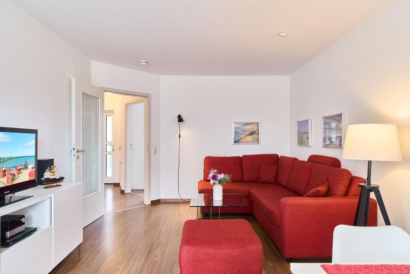 Wohnzimmer mit rotem Sofa, Glas-Tisch und Fernseher auf weißem Schrank.