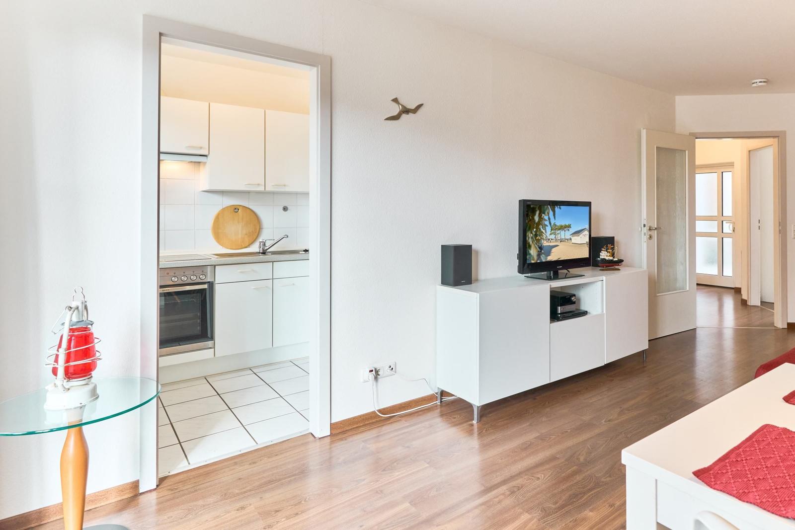 Wohnzimmer mit TV, Küchenbereich und Schlafzimmer im Hintergrund.