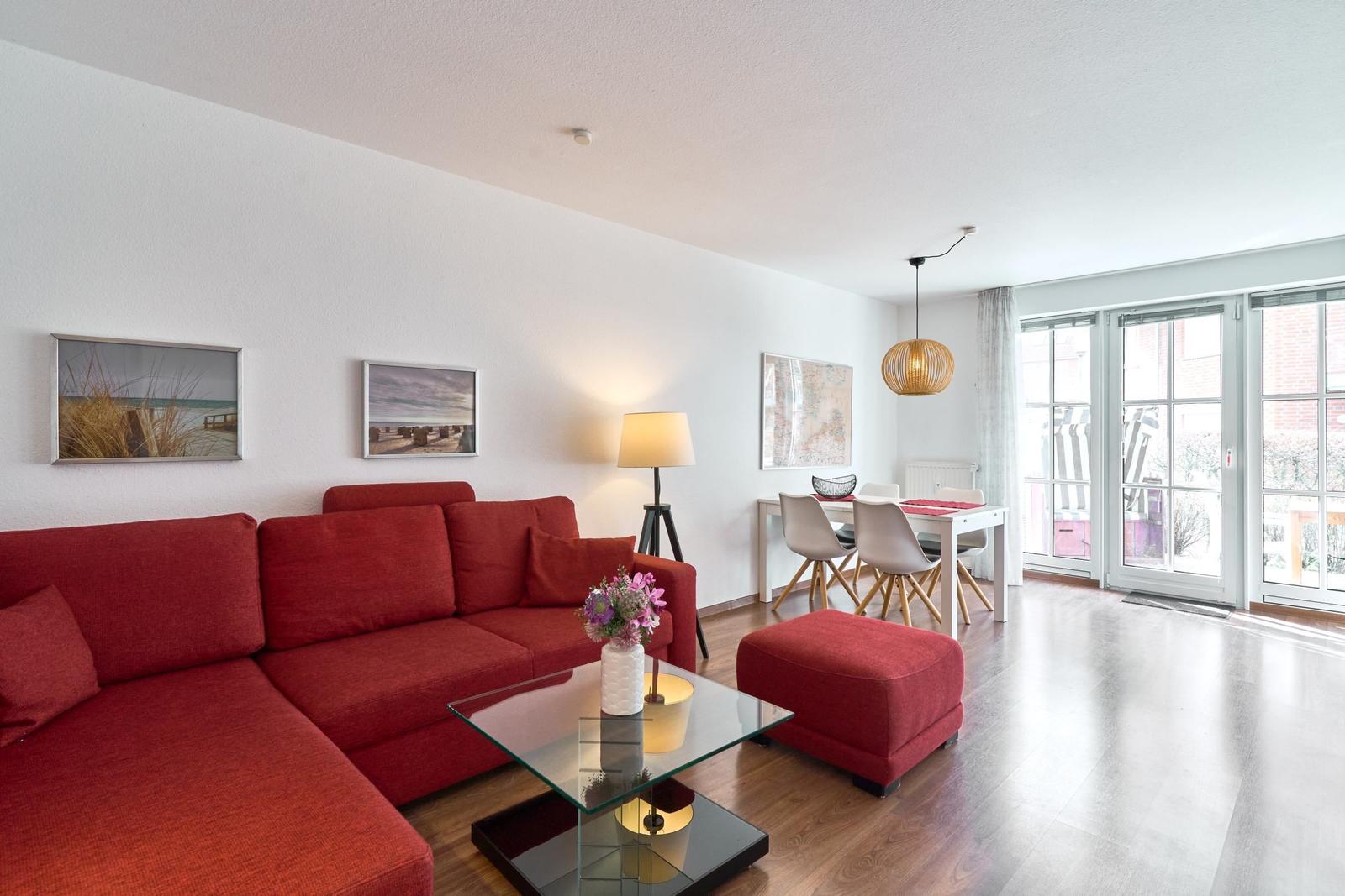 Wohn- und Essbereich mit rotem Sofa, Glas-Tisch und Terrassentür.