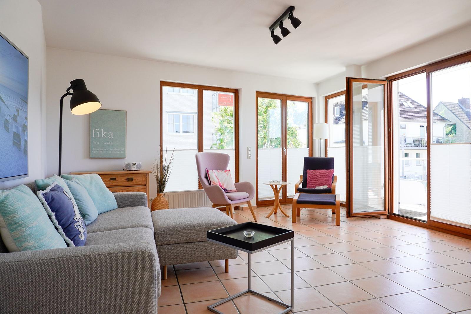 Wohnzimmer mit Sofa, zwei Sesseln und großem Fensterblick auf Balkon.