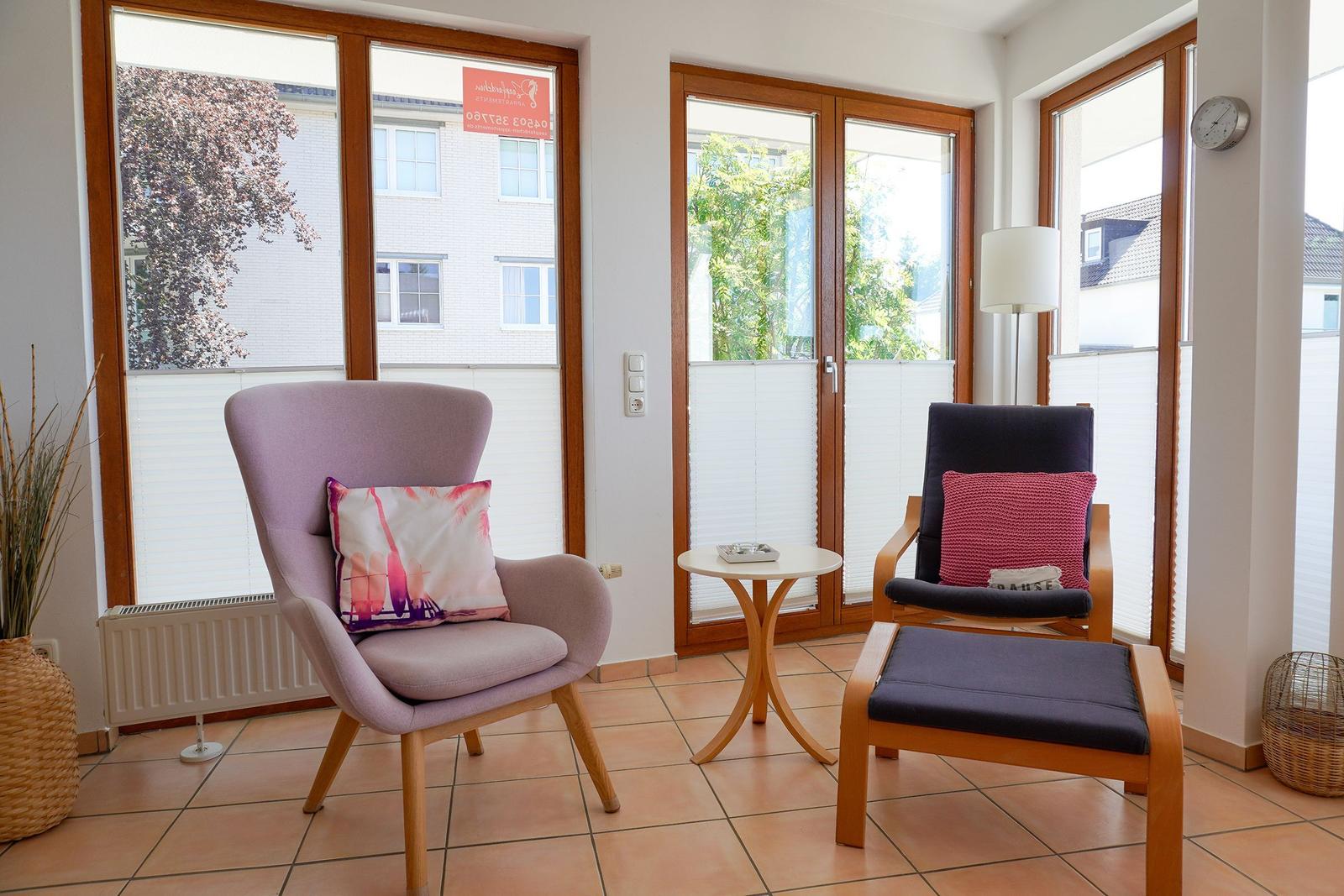 Zwei Sessel mit Kissen, kleiner Tisch und große Fenster mit Blick auf Außenbereich.