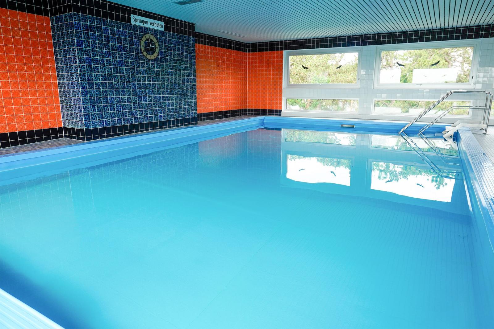 Innenpool mit blau-orangen Fliesen und Glasfenstern zur Außensicht.
