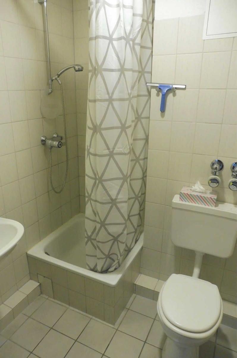Badezimmer mit Dusche, Toilette und Waschbecken. Duschvorhang mit geometrischem Muster.