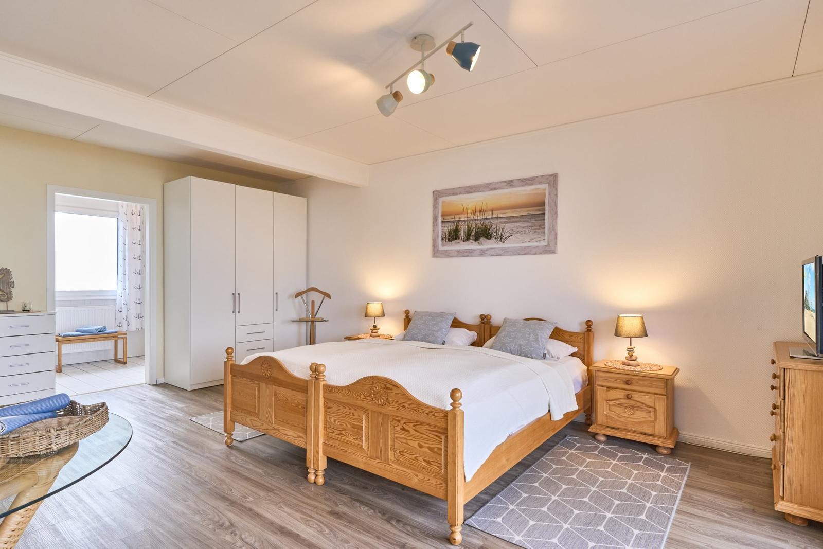 Schlafzimmer mit Holzbett, Nachttischen und Kleiderschrank. Wandbild und Teppich sind sichtbar.