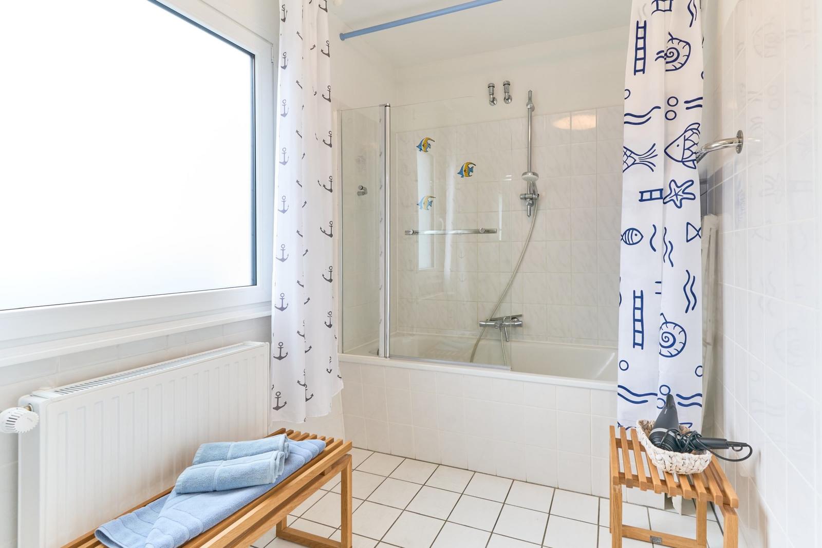 Badezimmer mit Dusche, Fenster und Holzregal mit Handtüchern.