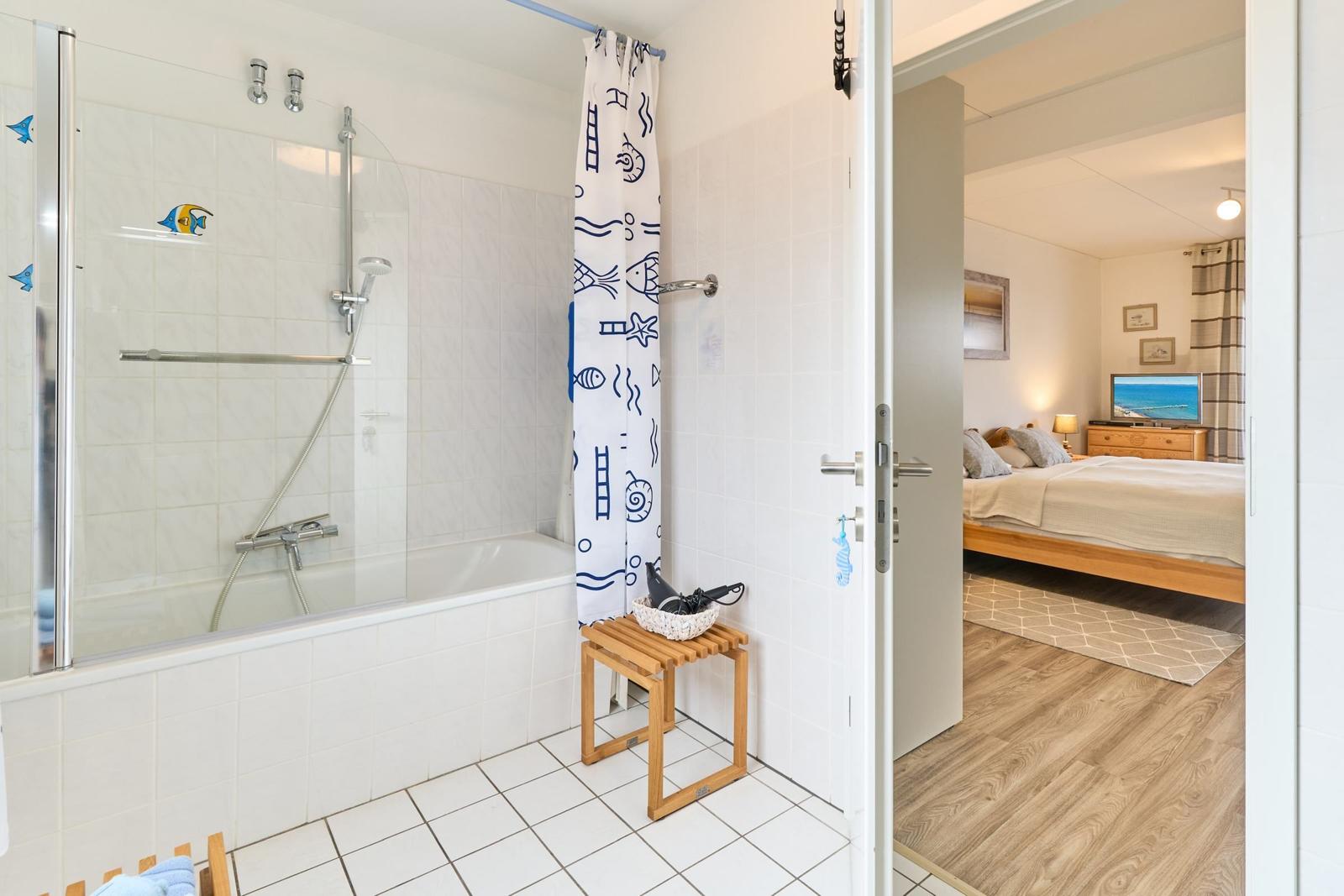 Badezimmer mit Dusche und Badewanne, daneben Schlafzimmer mit Bett und Fernseher.