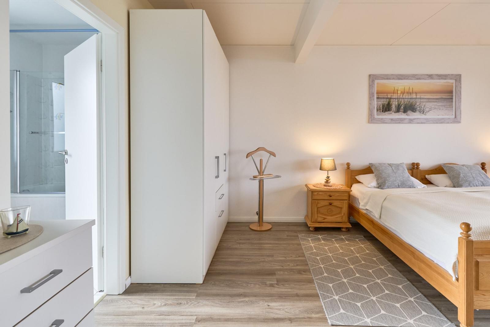 Schlafzimmer mit Bett, Nachttisch, Kleiderständer und integriertem Schrank. Badezimmer ist angrenzend.