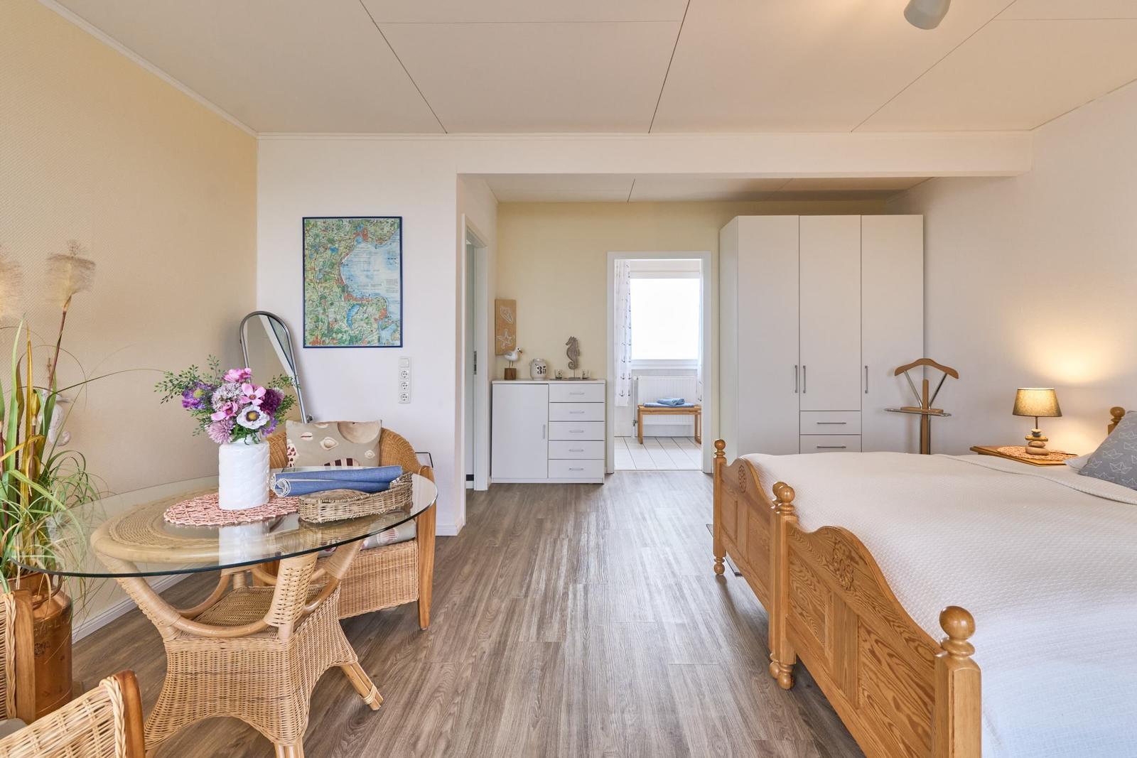 Schlafzimmer mit Holzbett, Kleiderschrank und Essbereich mit Glasplatte.