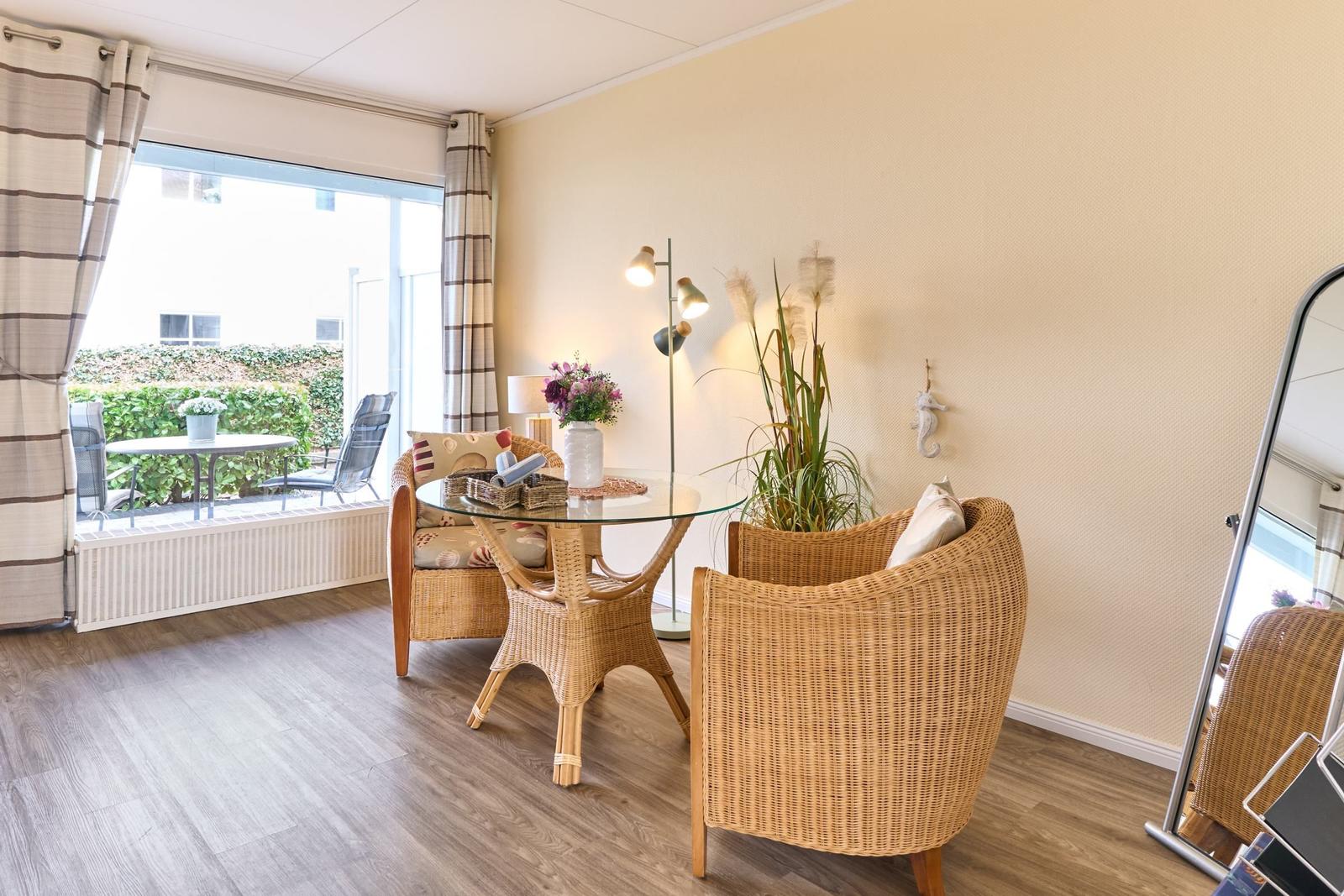 Wohnraum mit Rattanmöbeln, Glas-Tisch und Fenster zur Terrasse.