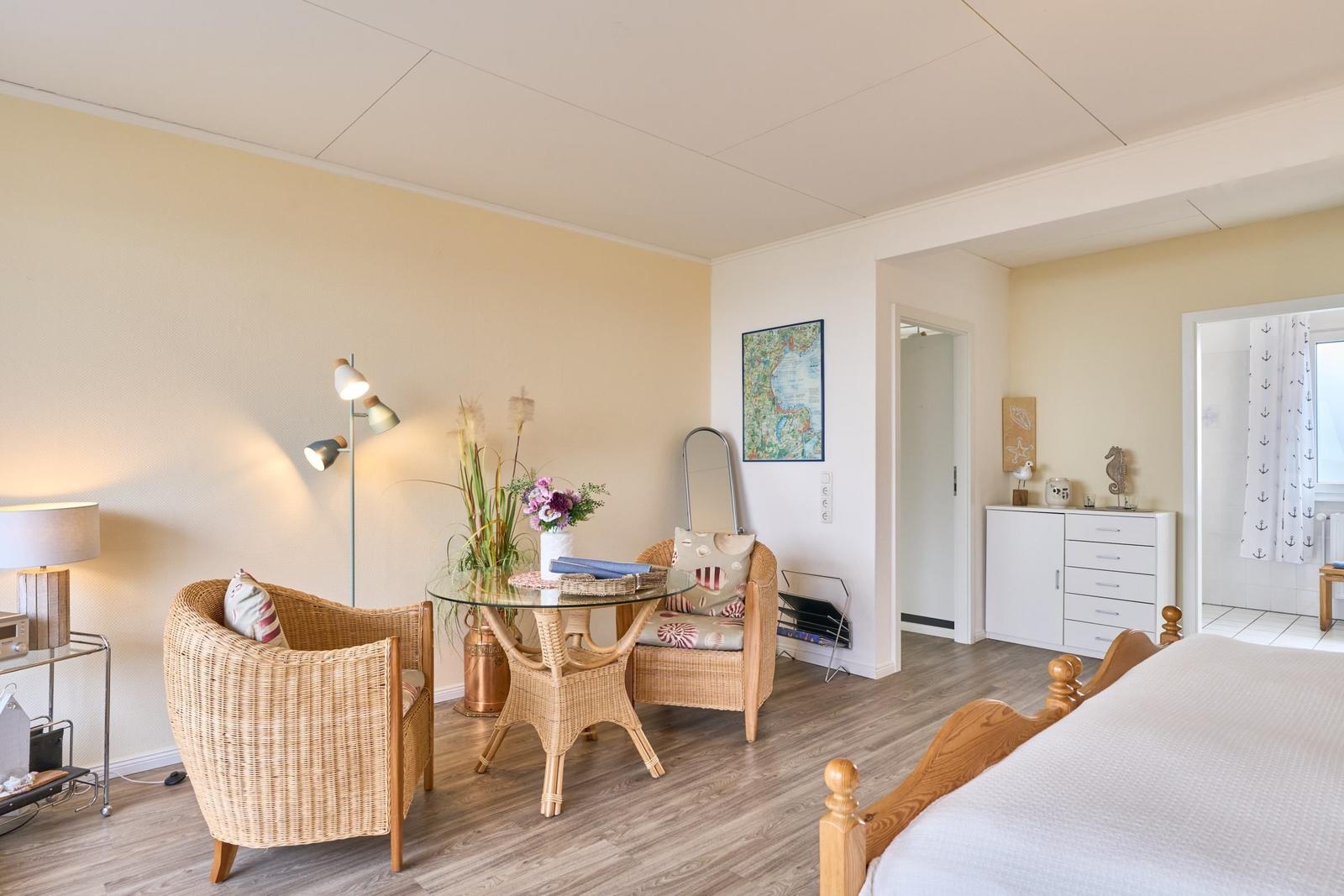 Ein Schlafzimmer mit Bett, Sitzgelegenheit und Tisch. Anschluss zur Badewanne.