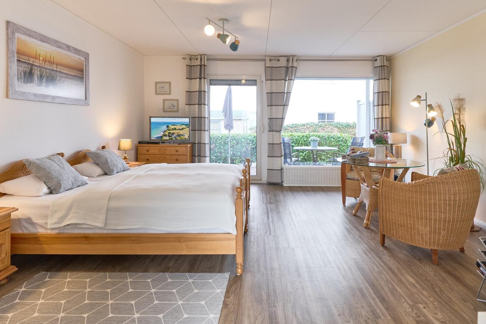 Schlafzimmer mit Bett, TV und Balkon mit Sitzgelegenheit.