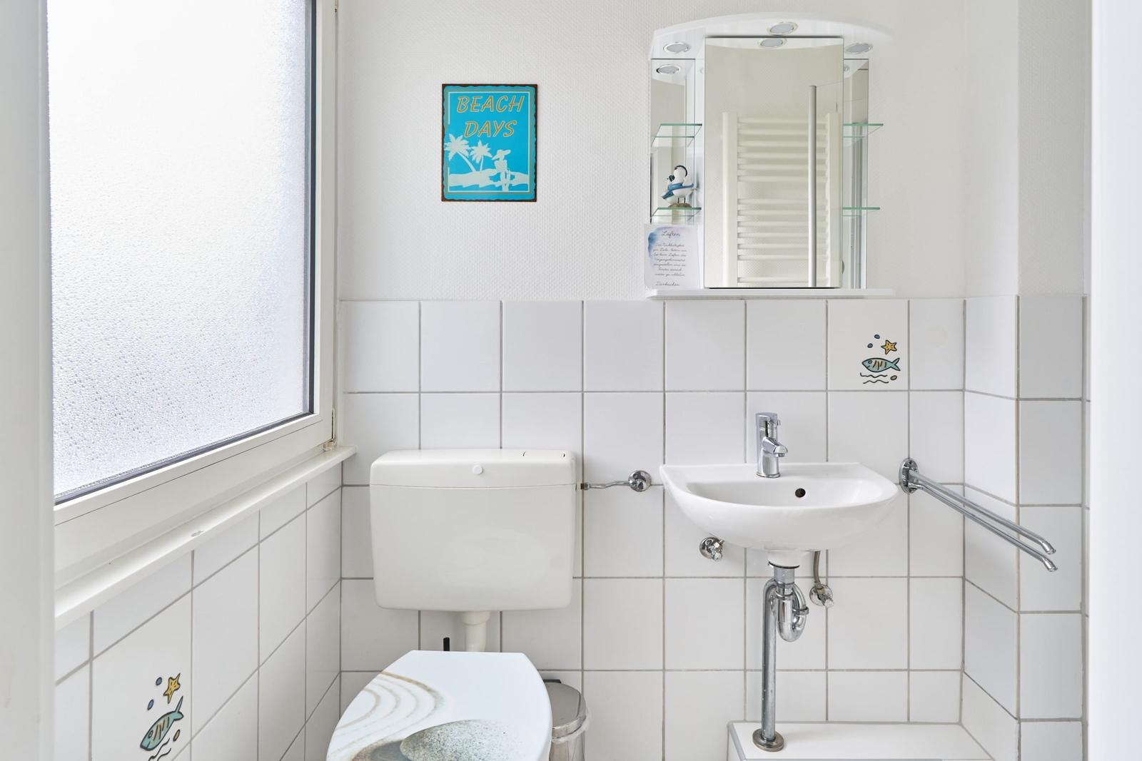 Badezimmer mit Toilette, Waschbecken und Spiegel. Fenster mit Milchglas.