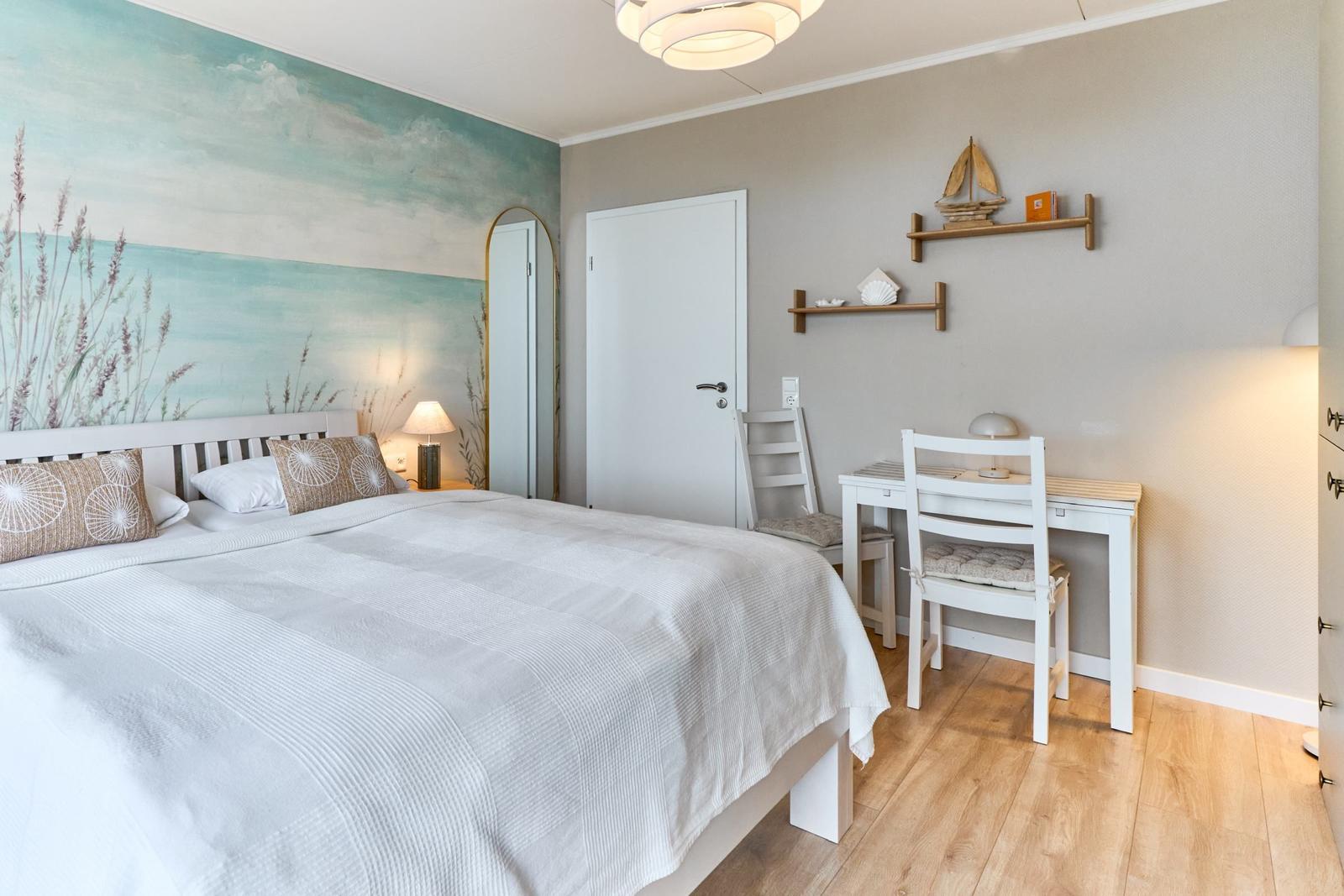 Schlafzimmer mit Bett, Schreibtisch und Wandbild. Holzboden und weiße Möbel.