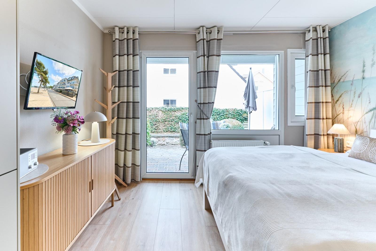 Schlafzimmer mit Bett, TV und Balkon. Holzoberfläche und gestreifte Vorhänge.