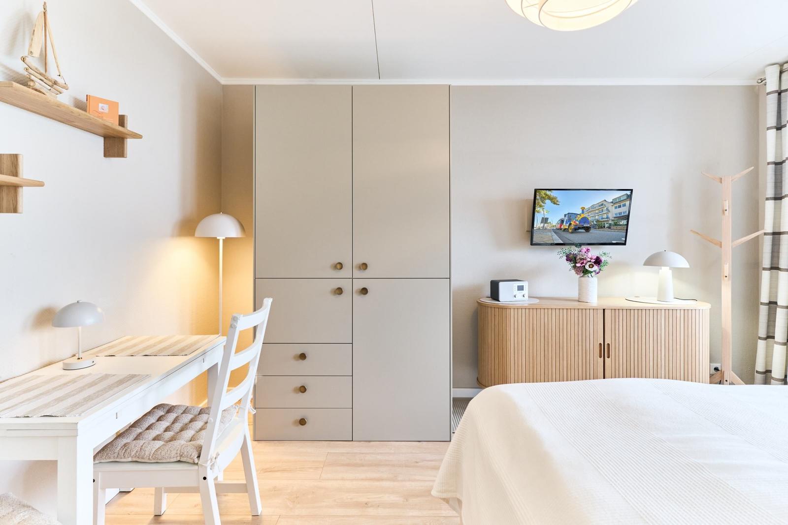 Schlafzimmer mit Schreibtisch, Kleiderschrank und Fernseher an der Wand.