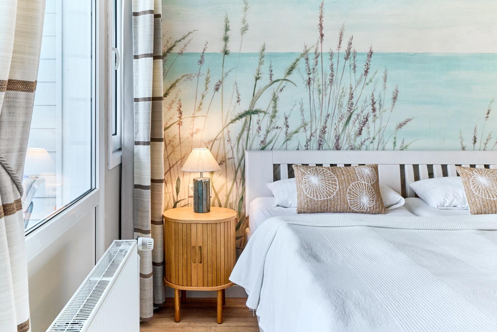 Schlafzimmer mit Bett, Nachttisch und Wandtapete mit Strandmotiv.