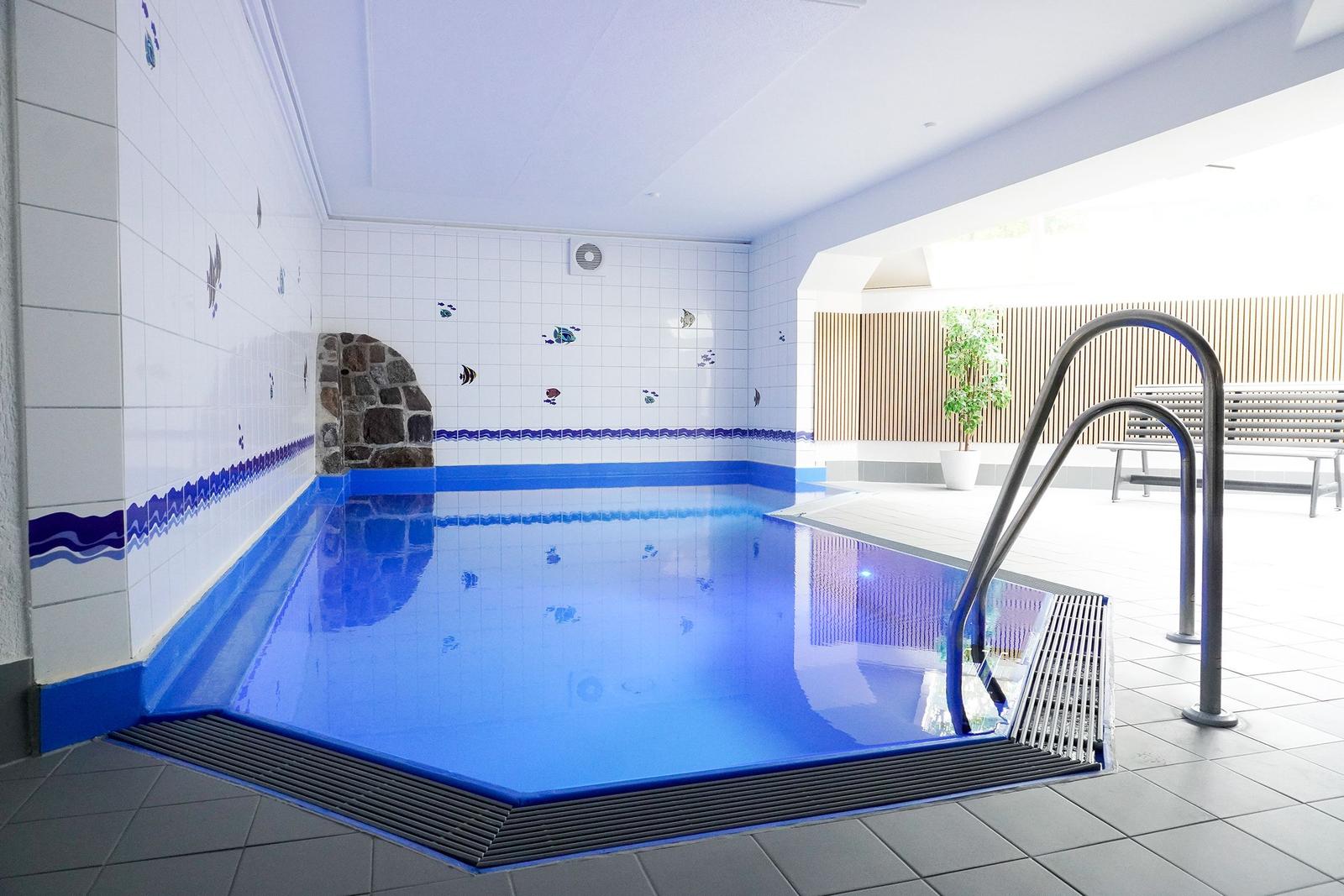 Innenpool mit blauer Fliesenwand und Metalltreppe