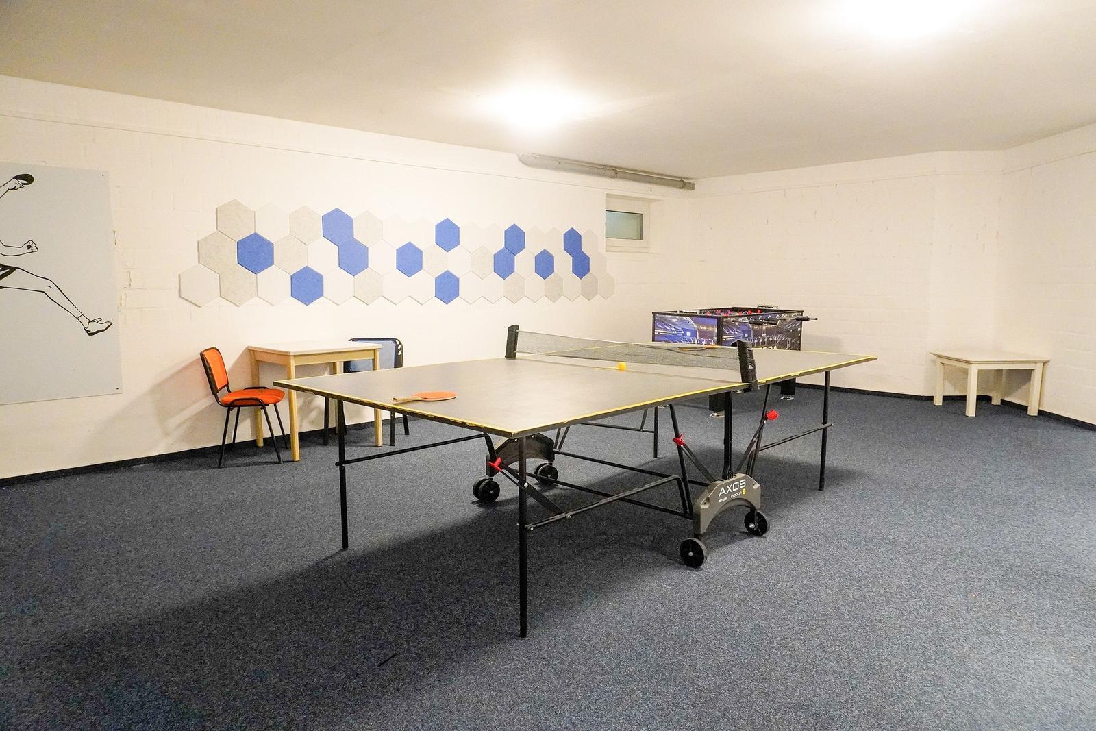 Raum mit Tischtennisplatte, Tisch, Stühle und Wanddekoration.