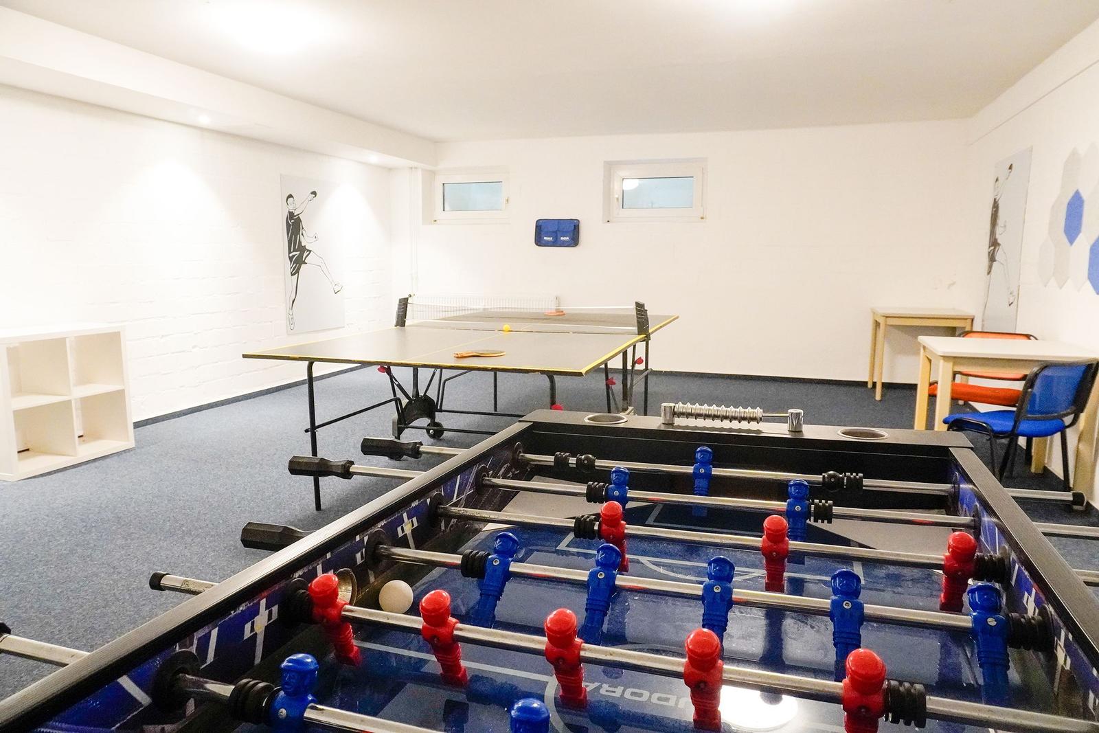 Raum mit Tischtennis- und Fußballtisch, Wandbilder und Sitzgelegenheiten.