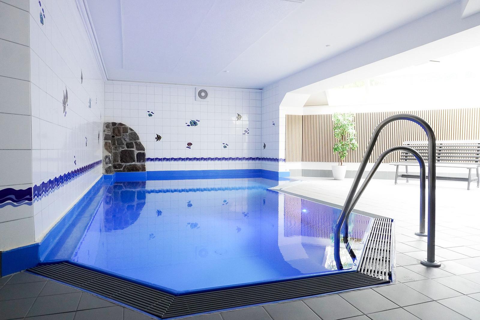 Innenpool mit blauer Wasserfläche, Wandfliesen und Metalltreppe zum Einsteigen.