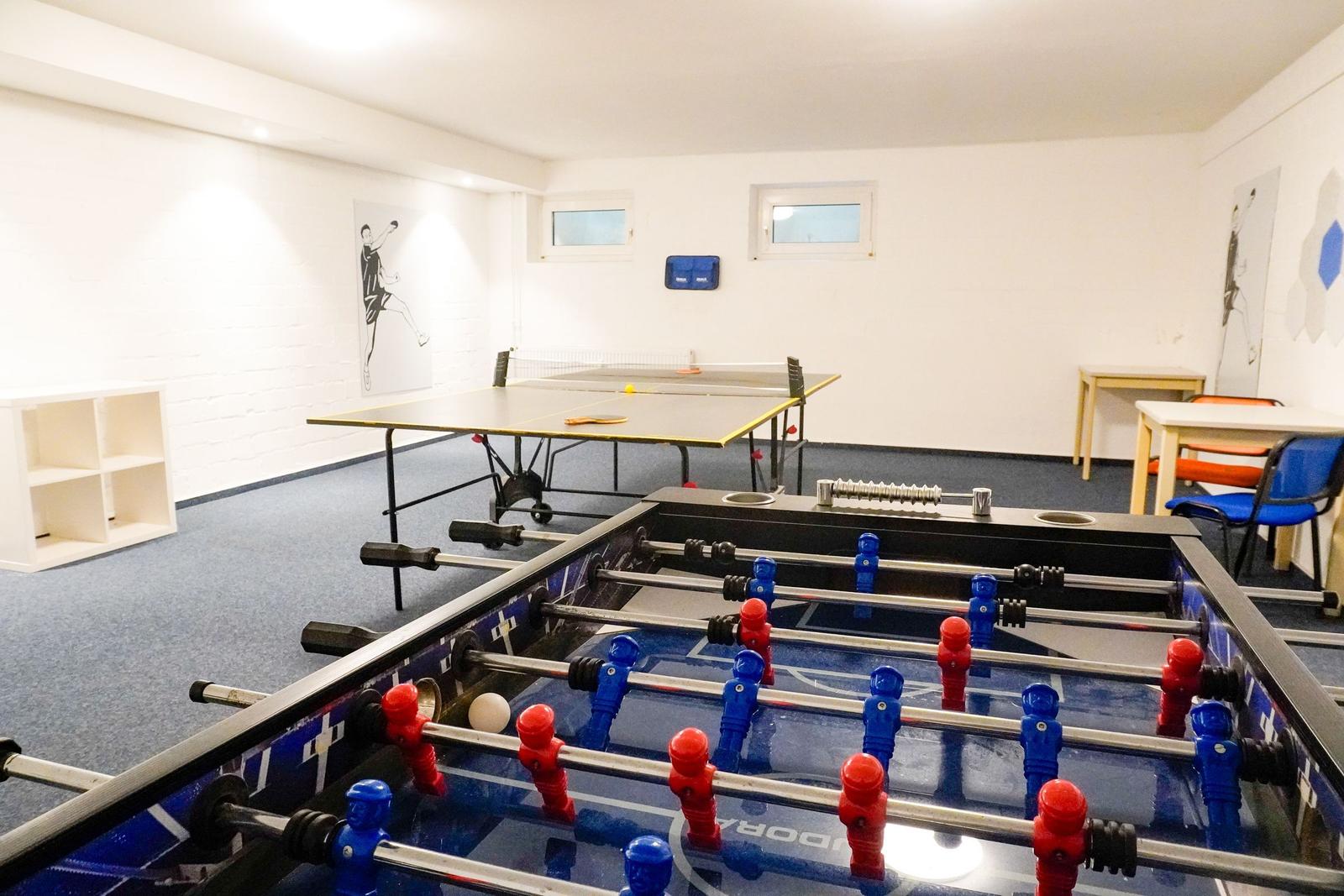 Raum mit Tischtennisplatte und Fußballtisch. An den Wänden hängen Bilder.